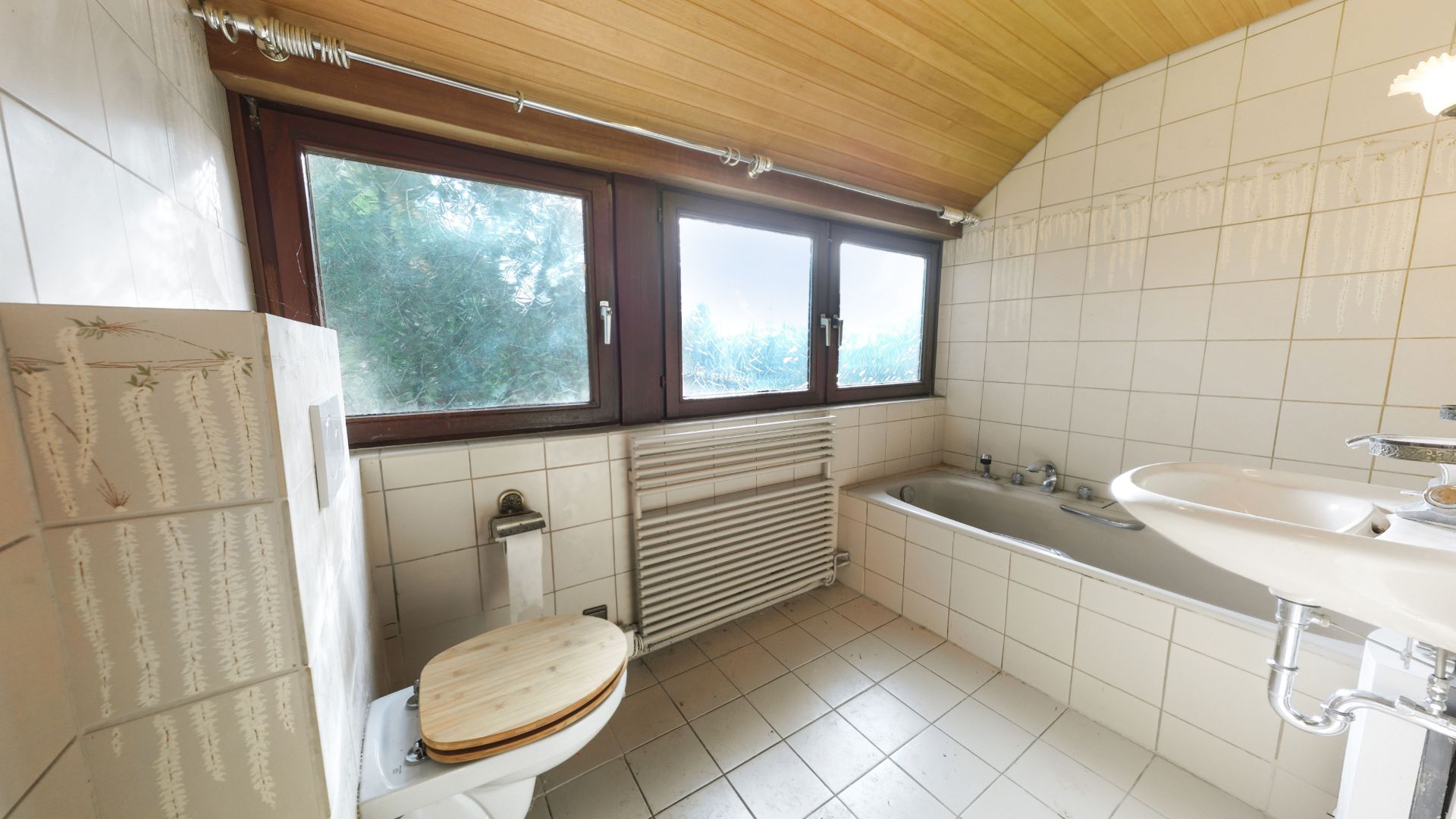 Helles Badezimmer mit Badewanne, WC, Waschbecken und drei großen Fenstern.