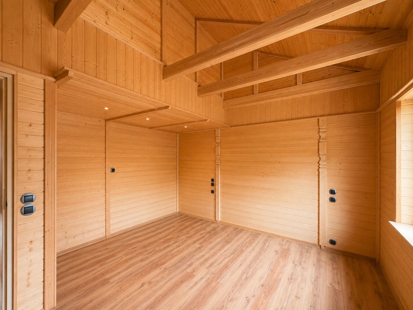 Leerer Raum mit Wänden, Decke und Boden aus hellem Holz und sichtbaren Balken.