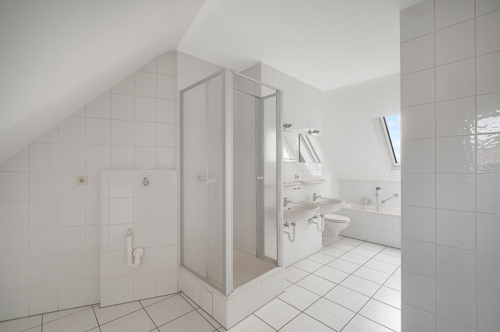 Helles Badezimmer mit Dusche, Badewanne, zwei Waschbecken und einem Fenster unter einer Schräge.