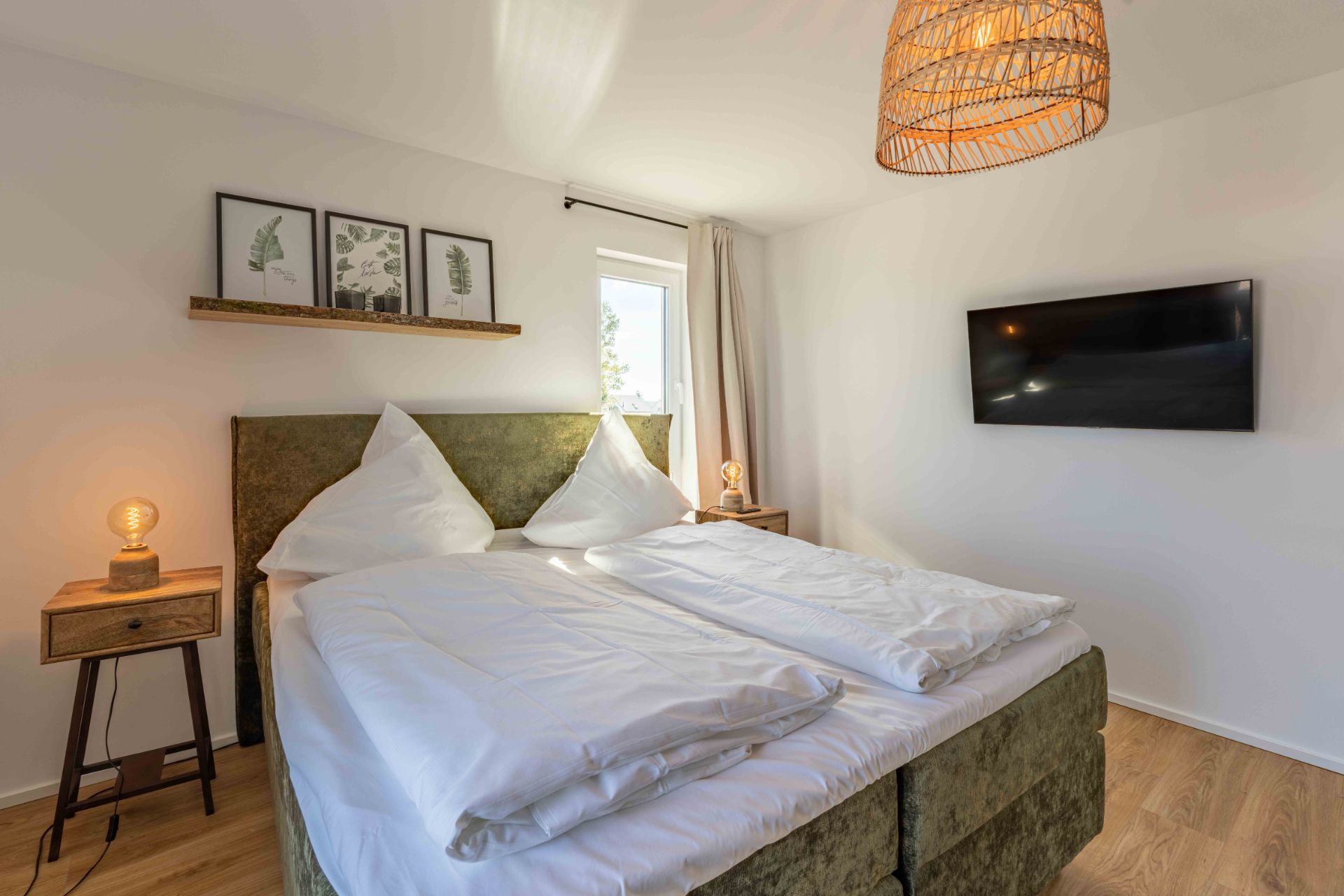 Helles Schlafzimmer mit Doppelbett, Nachttischen, Wandbildern und Flachbildfernseher an der Wand.
