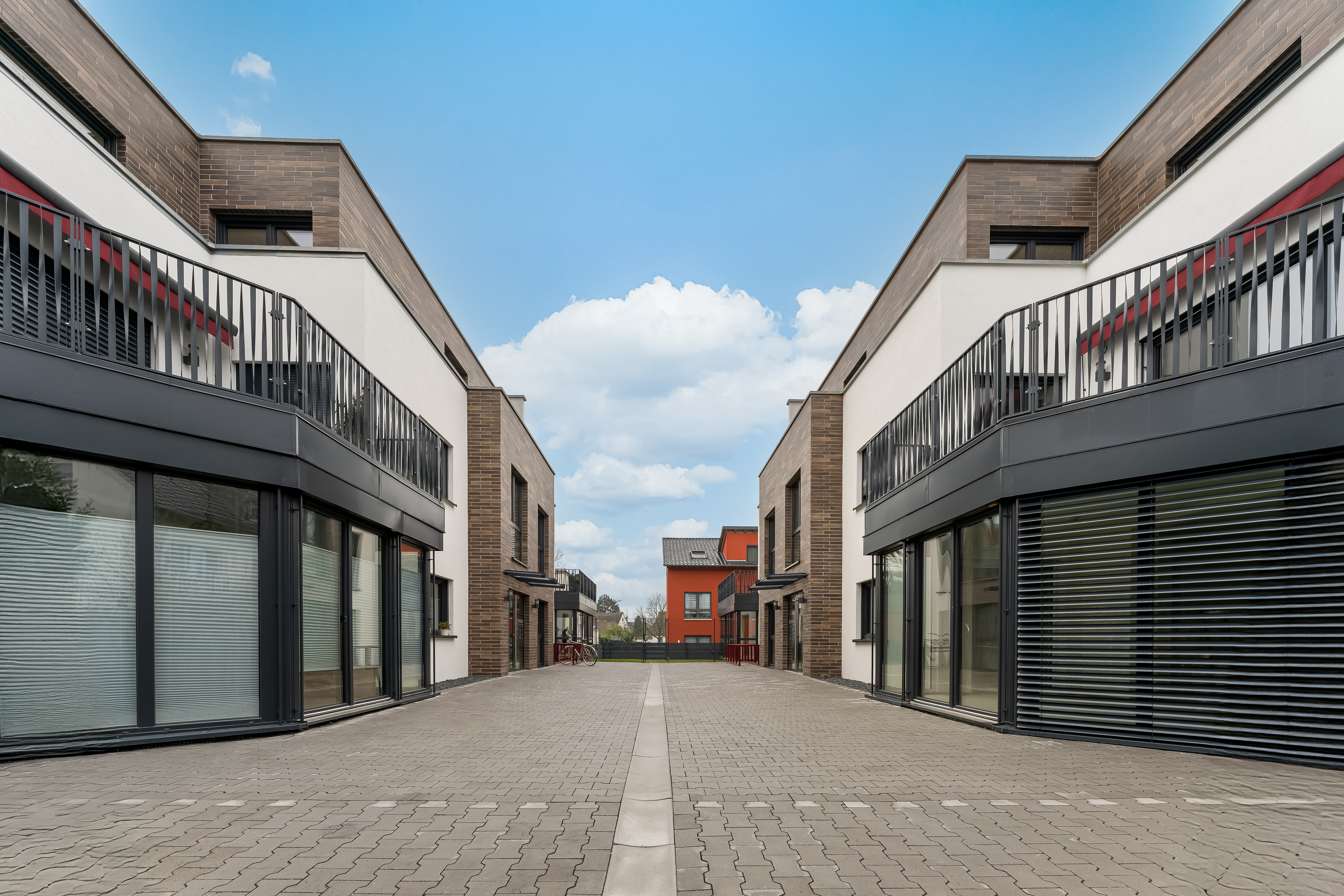 Moderne Wohngebäude mit großen Fenstern und gepflastertem Weg zwischen den Häusern.