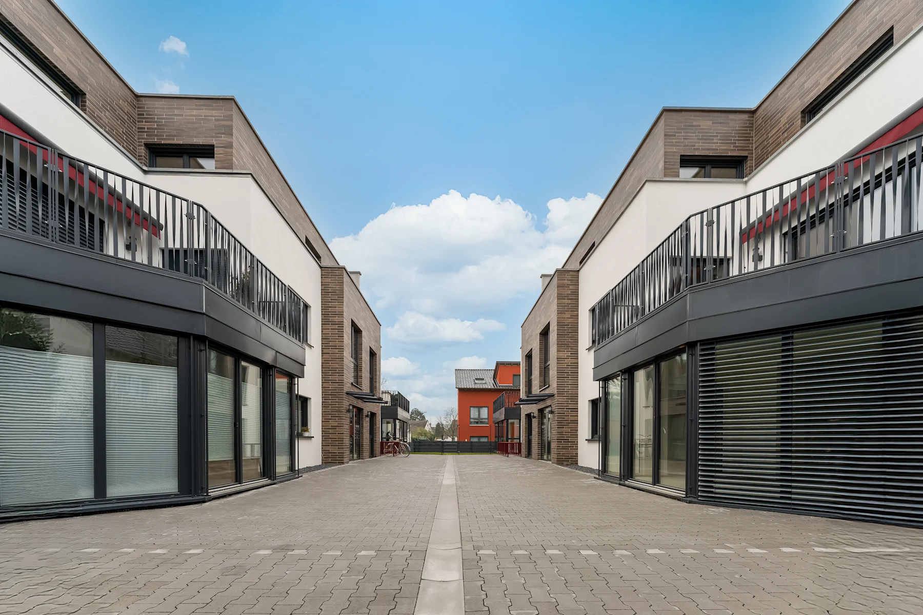Moderne Wohngebäude mit großen Fenstern und gepflastertem Weg zwischen den Häusern.