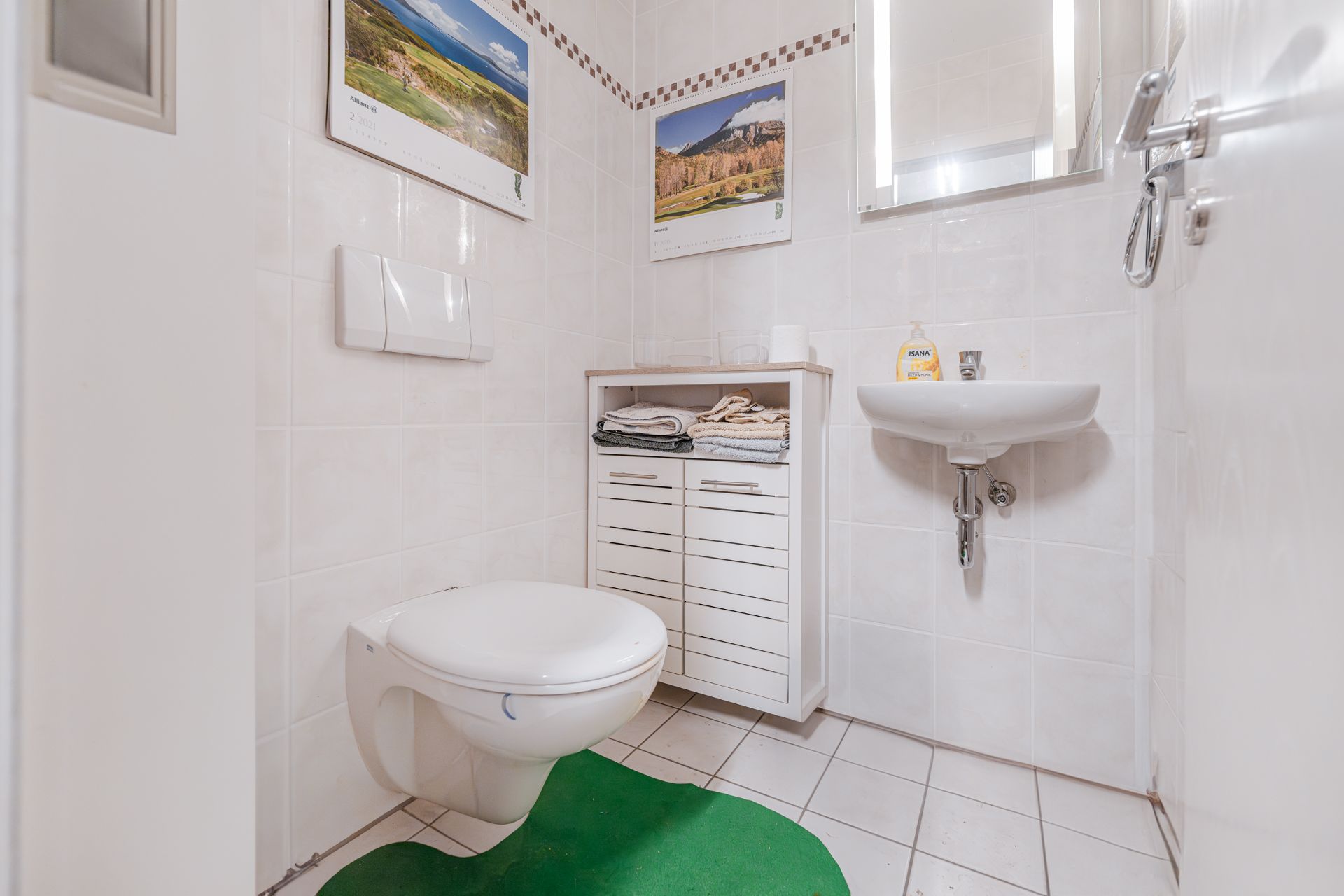 Kleines Badezimmer mit Wandtoilette, Waschbecken, Spiegel und weißem Schrank.