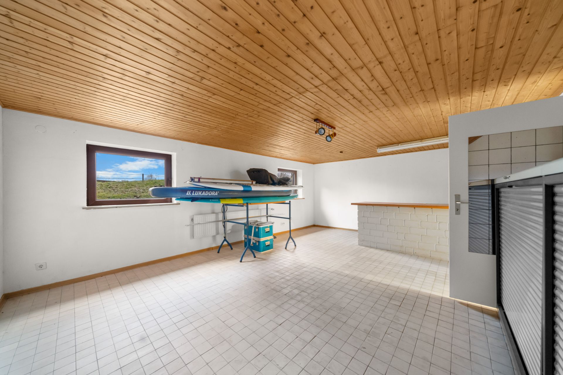 Heller Raum mit Holzdecke, Fenster, Wandtheke und einem Sportgerät auf Gestell.