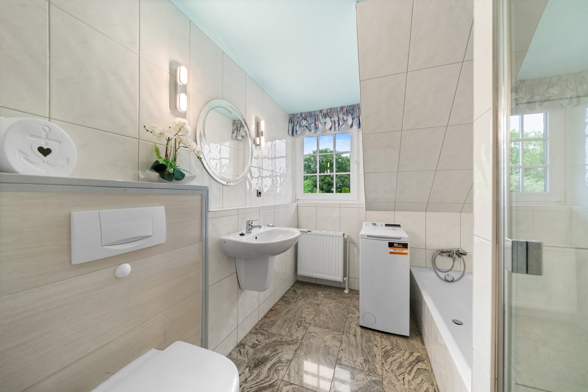 Helles Badezimmer mit Waschbecken, Toilette, Badewanne, Waschmaschine und Fenster.