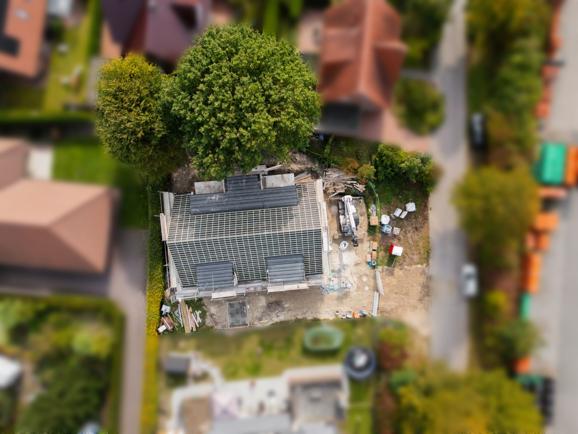 Luftaufnahme eines Wohnhauses im Bau mit Baum daneben und Baumaterial im Garten.
