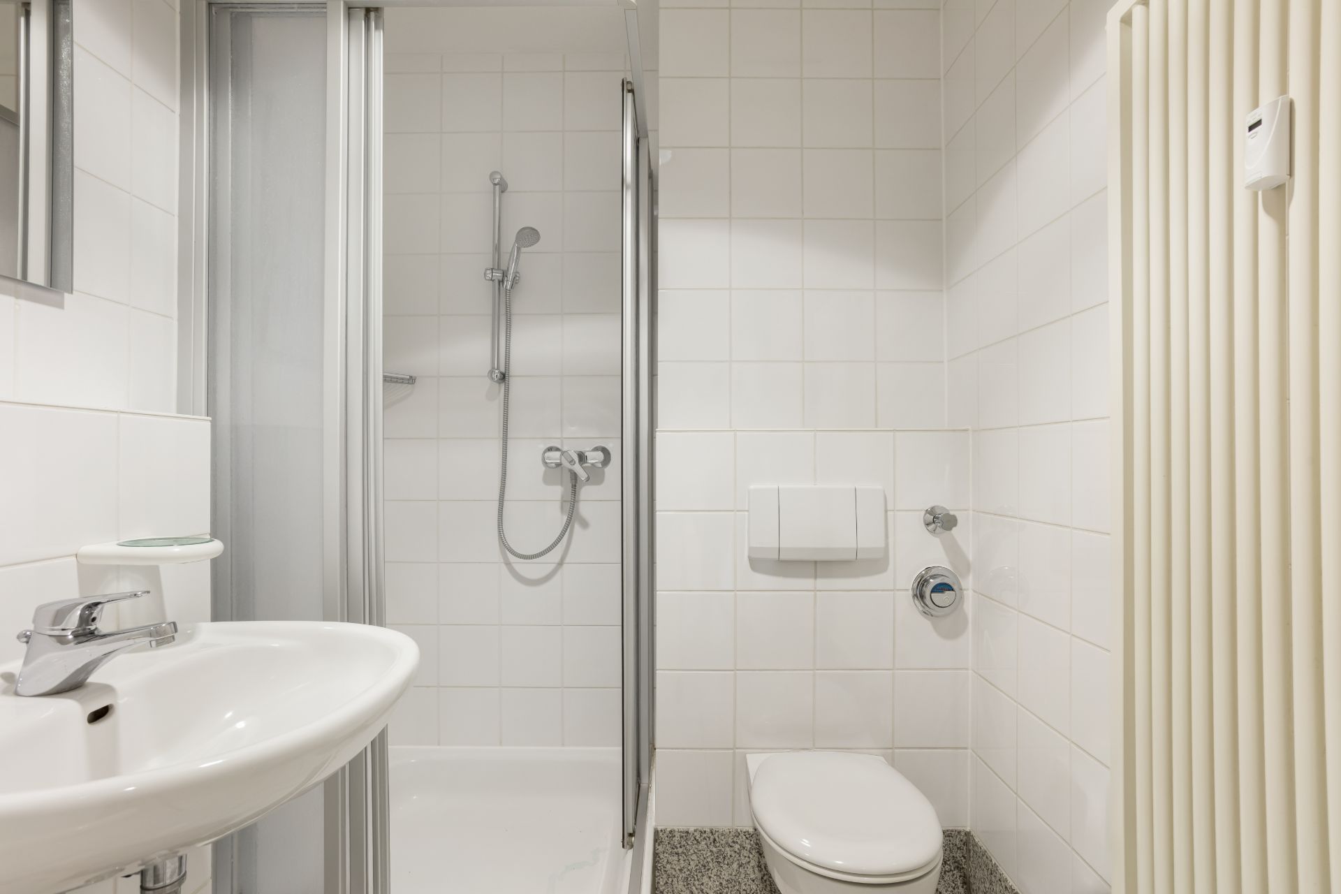 Modernes Badezimmer mit Dusche, Waschbecken, Toilette und Heizkörper, alles in weißen Fliesen.