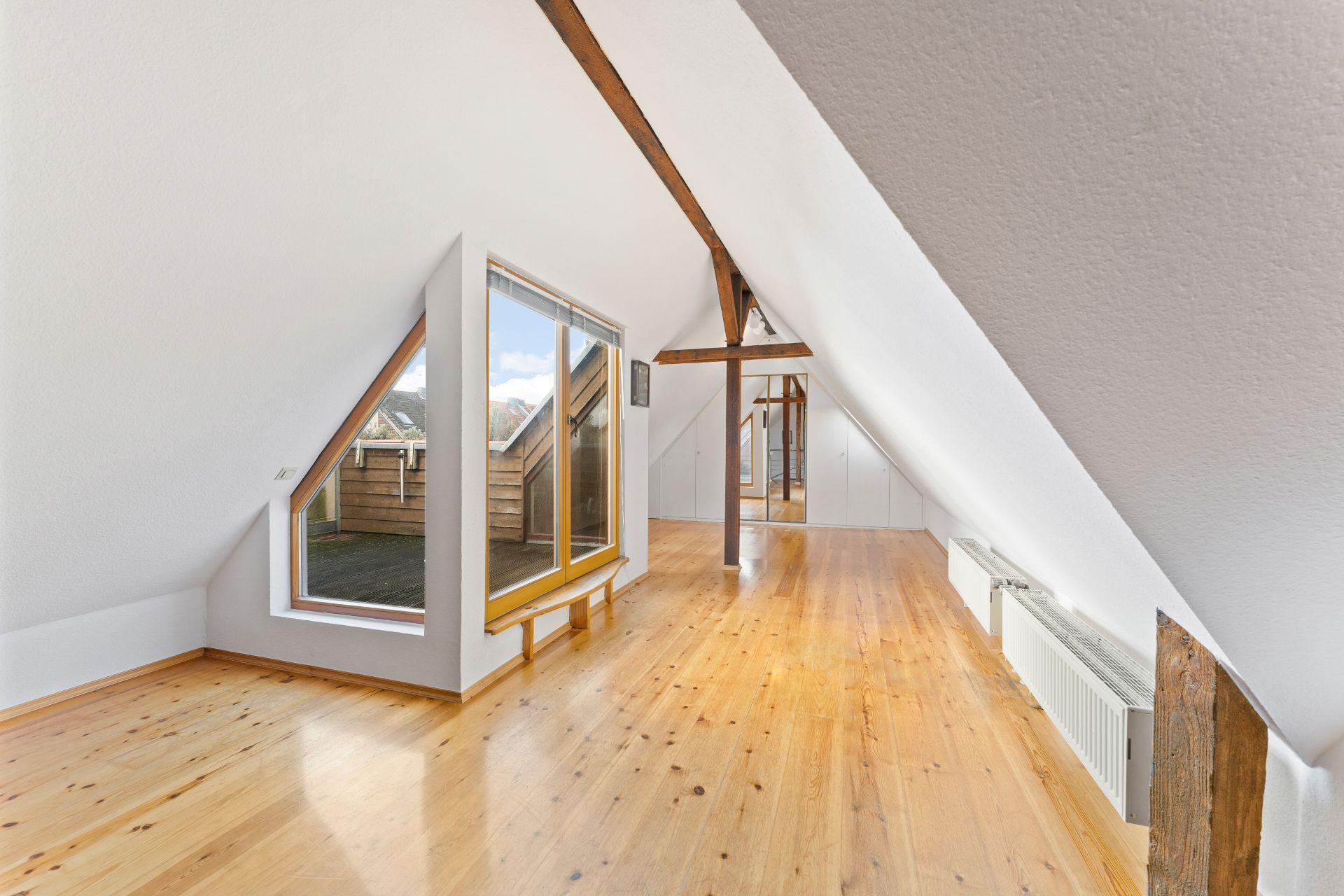 Heller Dachbodenraum mit Holzfußboden, sichtbaren Balken und großen Fenstern.