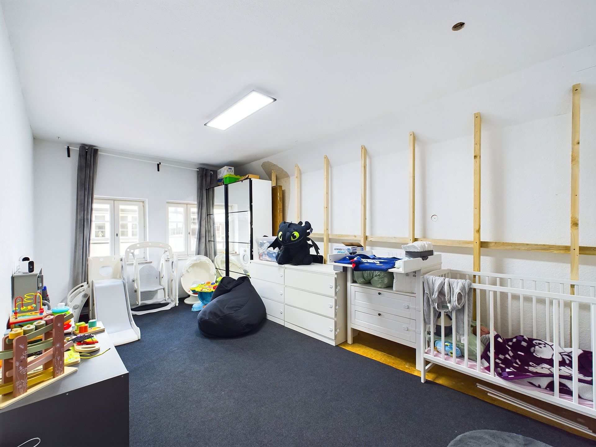 Kinderzimmer mit Spielzeug, Kleiderschränken, Wickelkommode, Sitzsack und Babybett.
