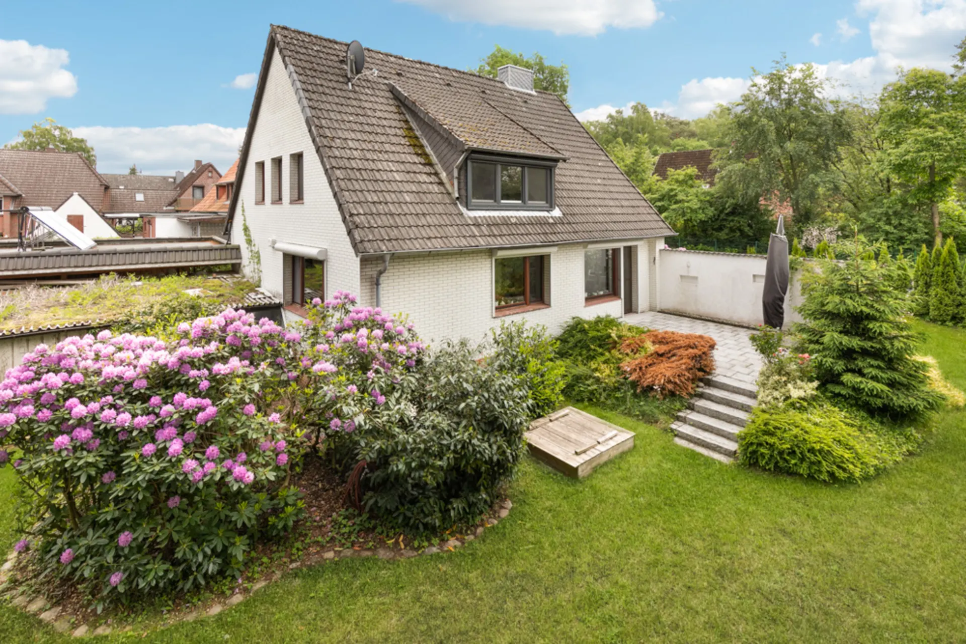 Weißes Einfamilienhaus mit Garten, bunten Blumen und Terrasse bei sonnigem Wetter.