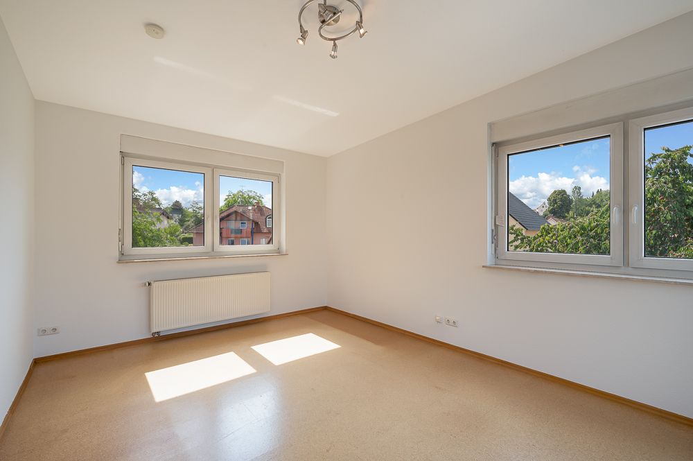 Heller, leerer Raum mit zwei Fenstern, hellem Boden und Heizkörper unter dem Fenster.