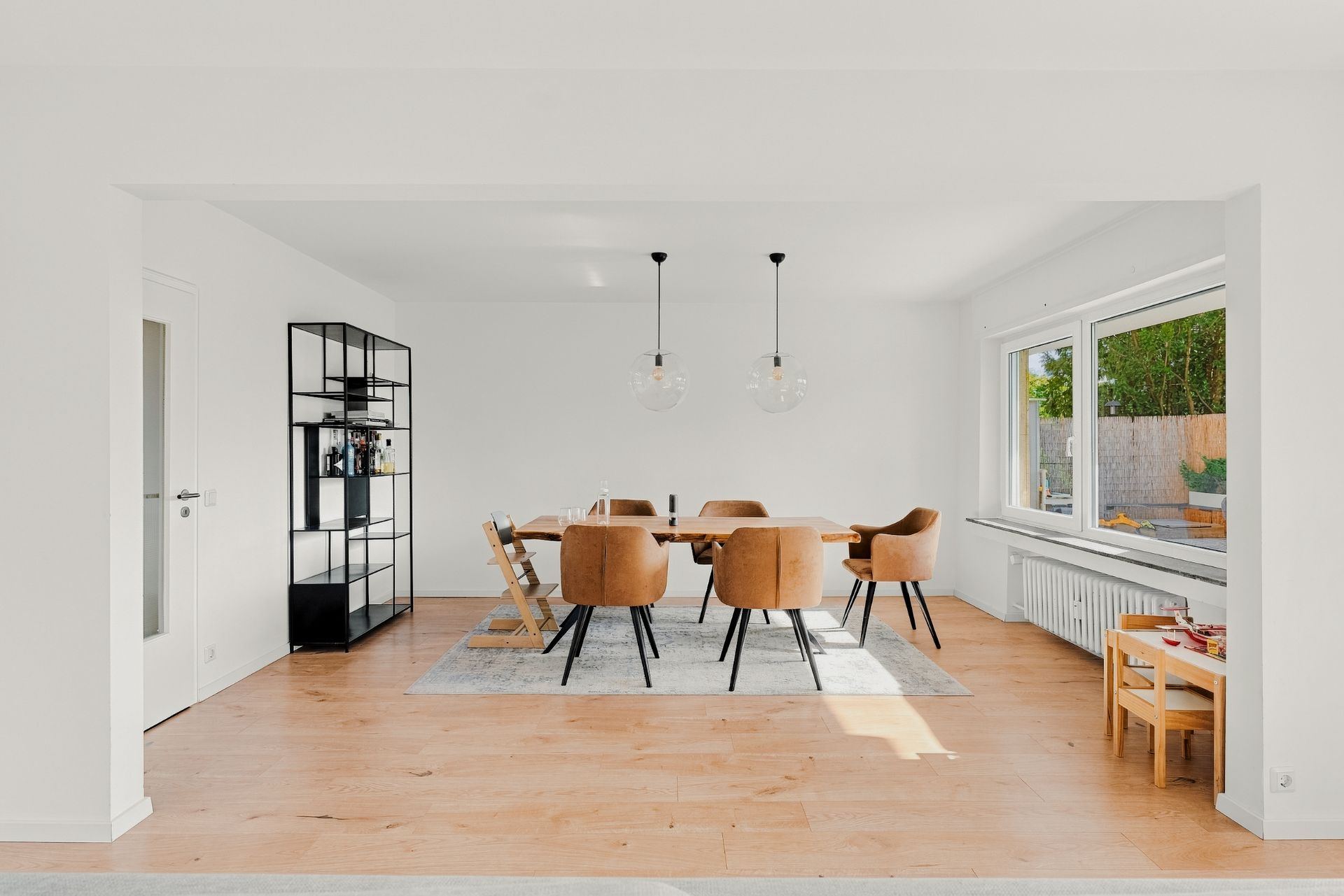 Helles Esszimmer mit Holzboden, großem Tisch, sechs Stühlen, Regal und großen Fenstern.