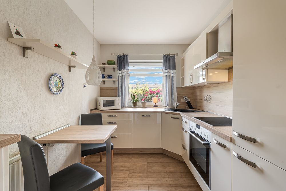 Helle Einbauküche mit Esstisch, Stühlen und Fenster mit Blick nach draußen.