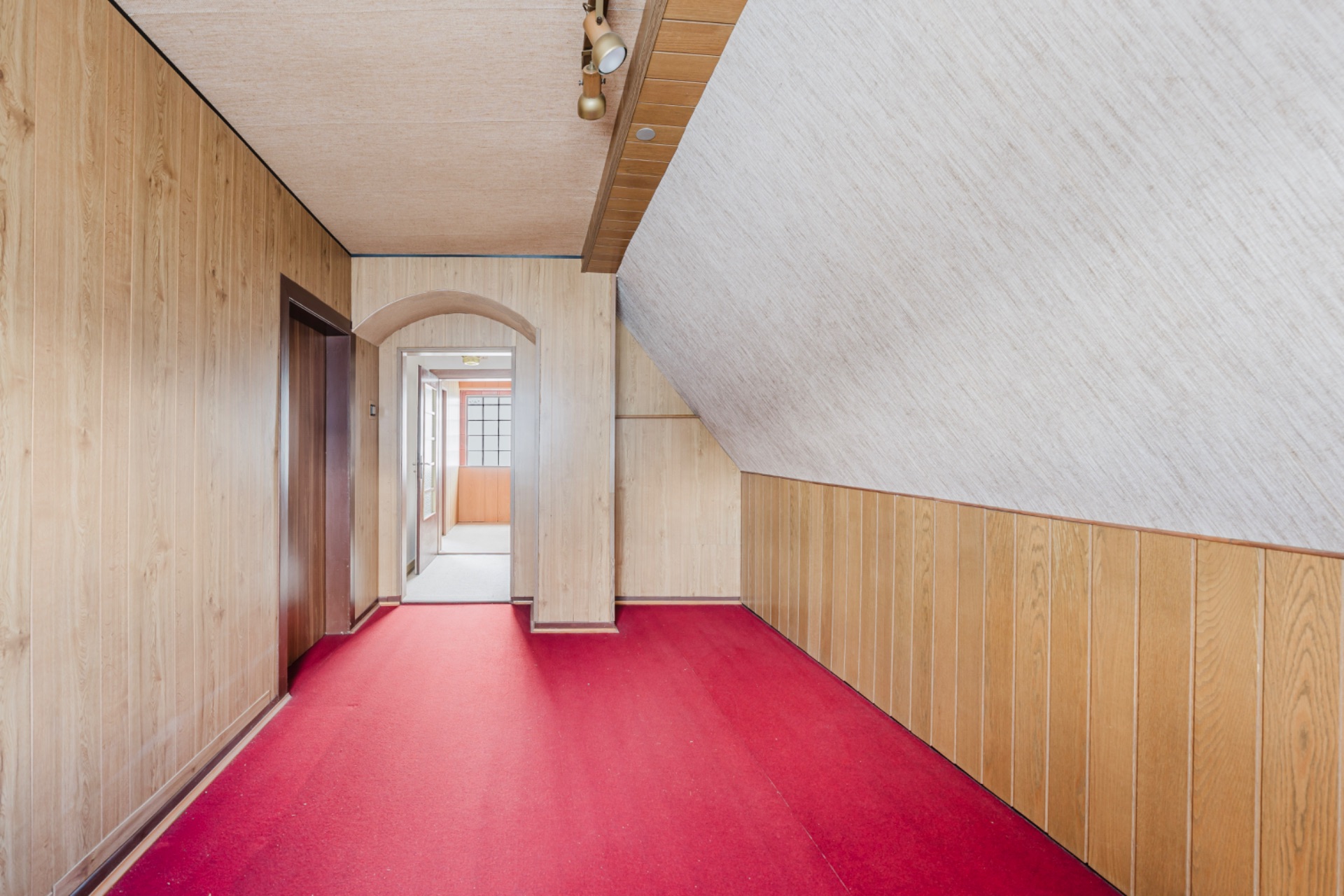 Flur mit rotem Teppich, Holzvertäfelung und schräger Decke, führt zu weiterem Raum.