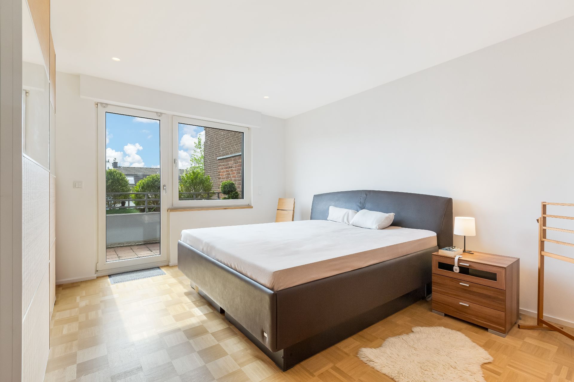 Helles Schlafzimmer mit großem Bett, Nachttisch, Lampe und Zugang zu einem Balkon.
