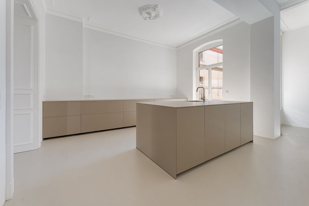 Moderne, helle Küche mit Kücheninsel und großen Schränken, Fenster im Hintergrund.