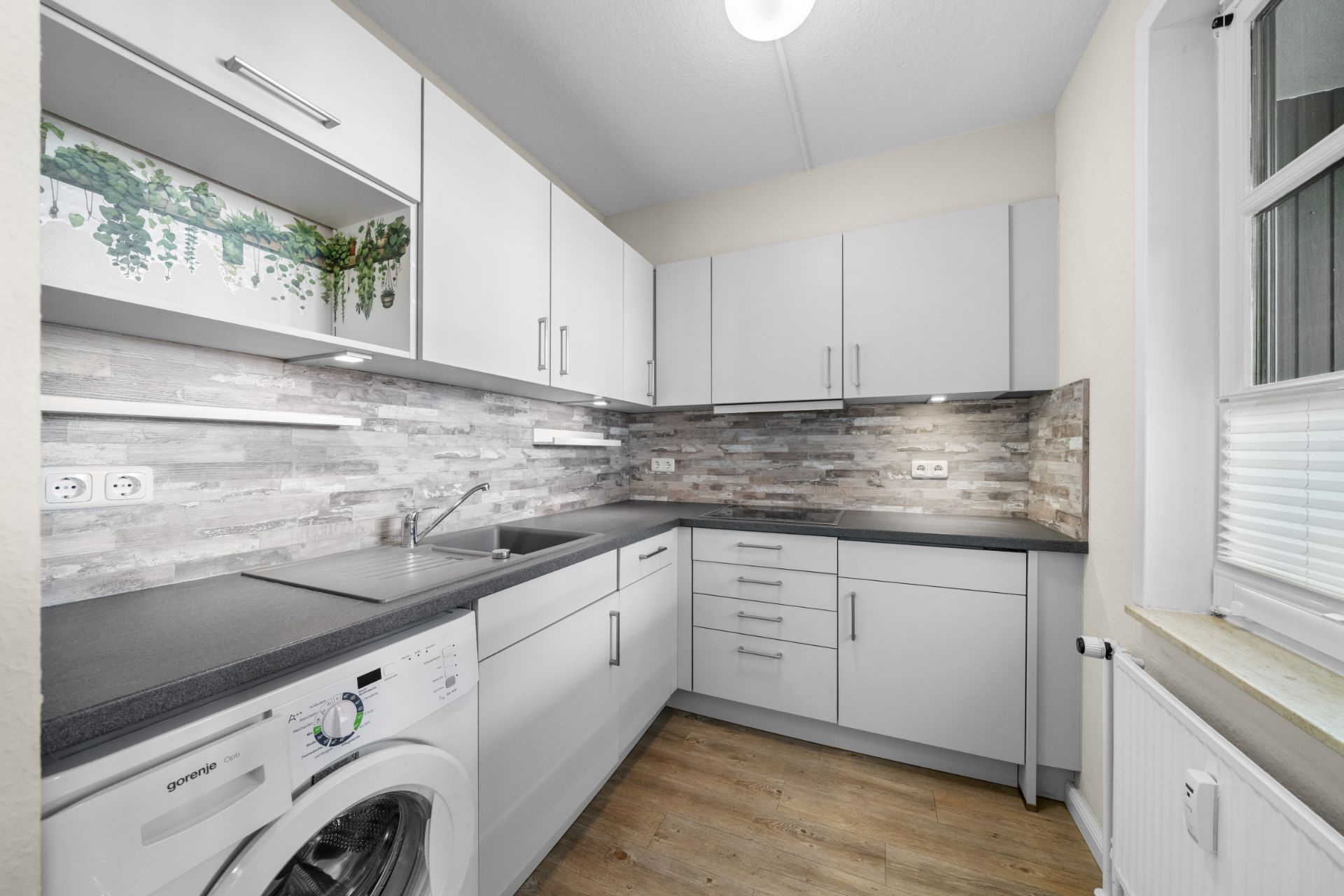 Moderne, helle Küche mit weißen Schränken, Waschmaschine und grauer Arbeitsplatte.