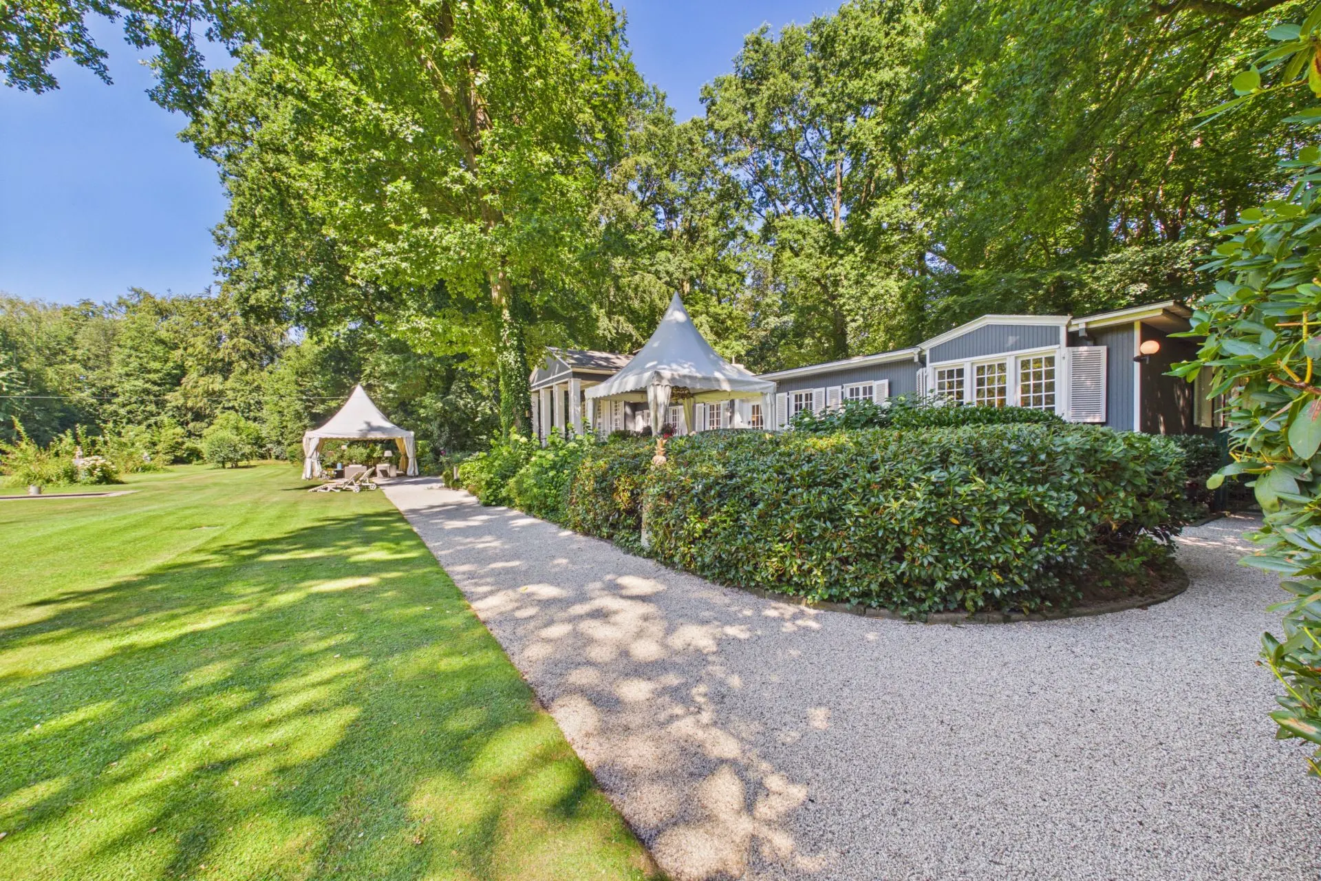 Gartenweg führt an einem grauen Haus mit weißen Fenstern und Gartenpavillon vorbei.
