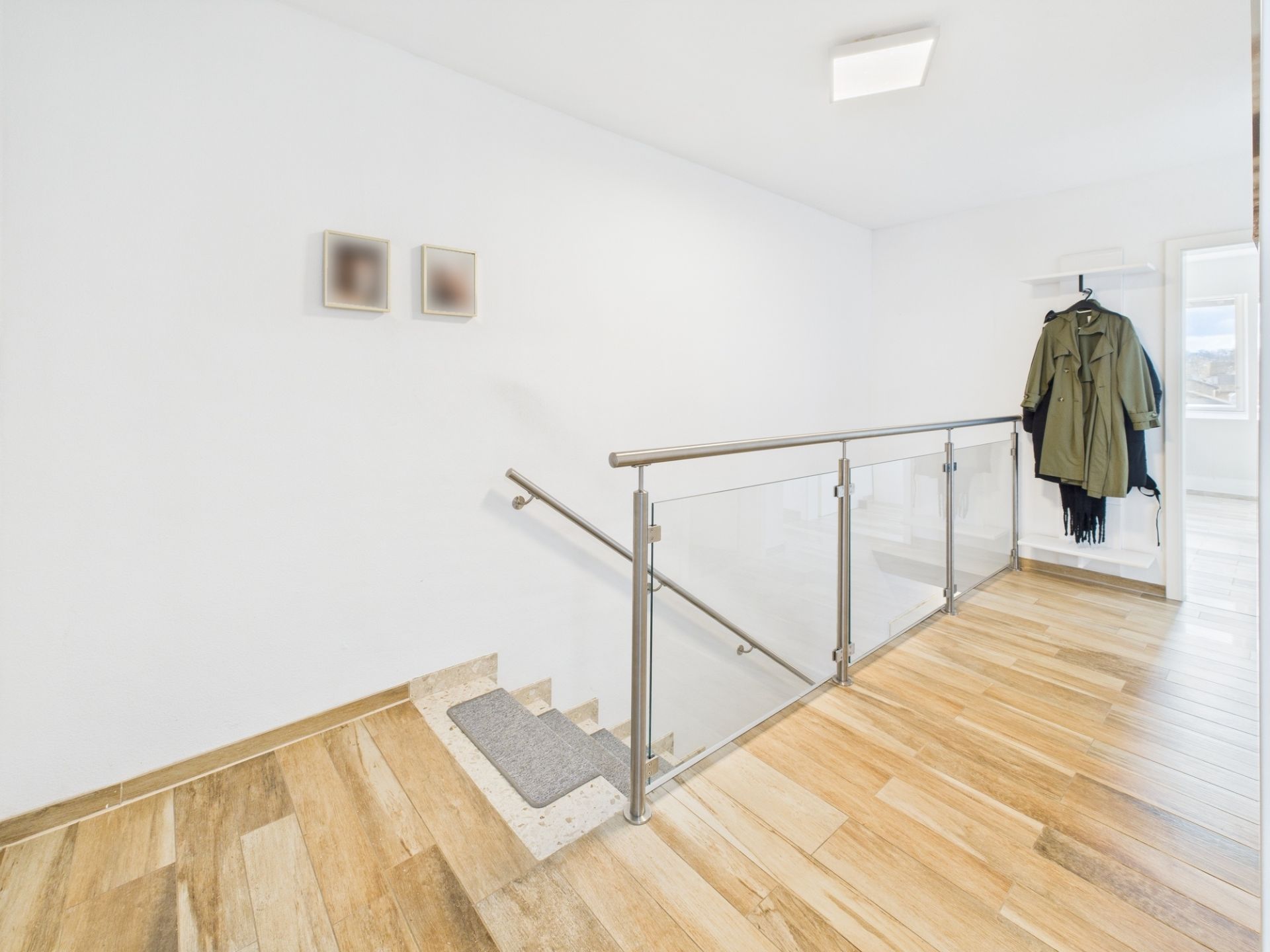 Heller Flur mit Holzfußboden, Glasgeländer und Garderobe mit Jacken an der Wand.