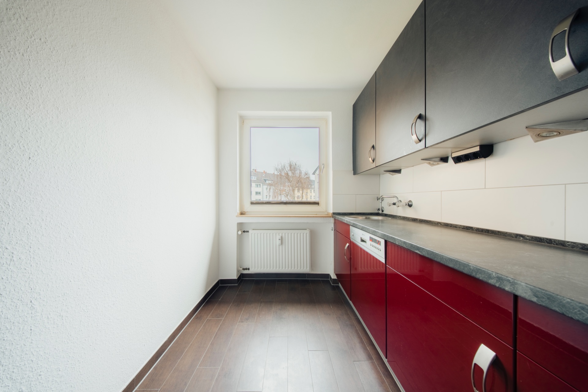 Schmale Küche mit dunklem Boden, roten Unterschränken, schwarzen Oberschränken und Fenster am Ende.