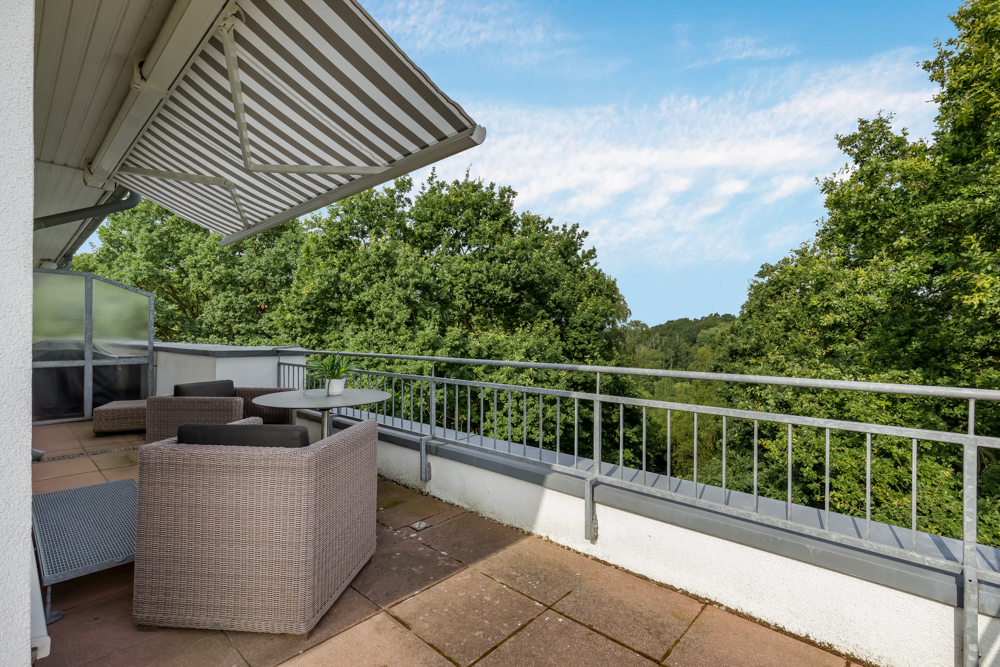 Große Terrasse mit Markise, Gartenmöbeln und Ausblick auf grüne Bäume.
