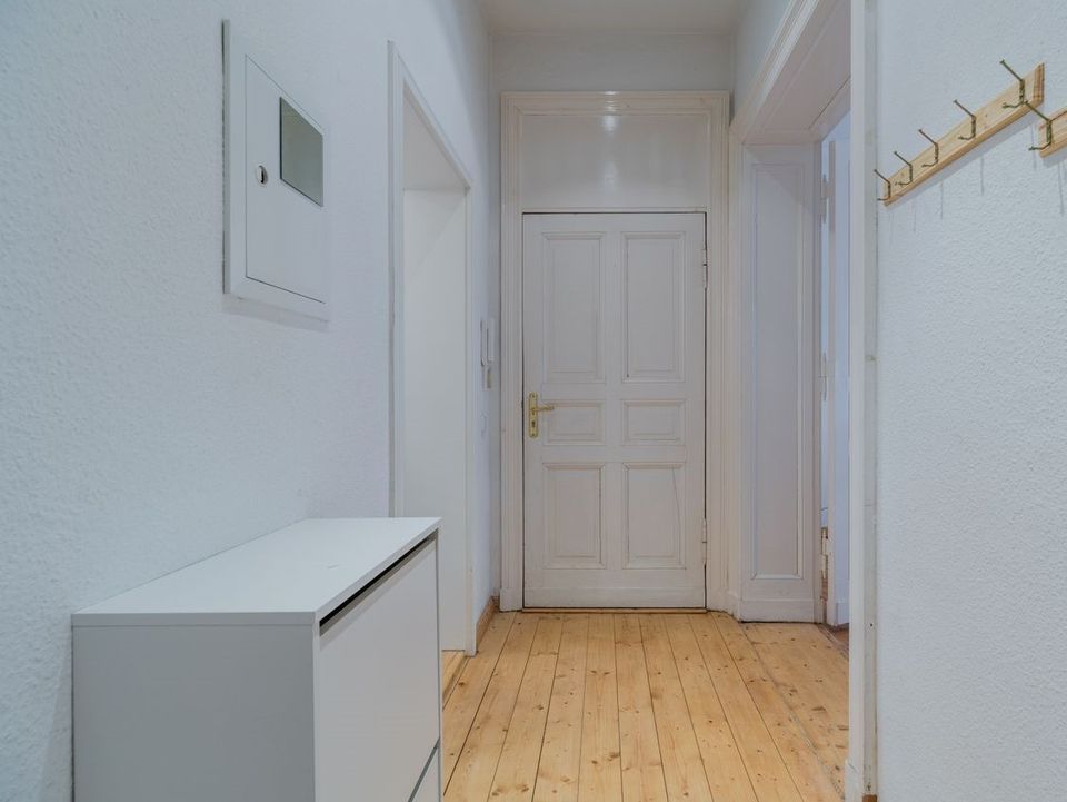 Heller Flur mit Holzboden, weißer Tür, Schuhschrank und Holzgarderobe an der Wand.