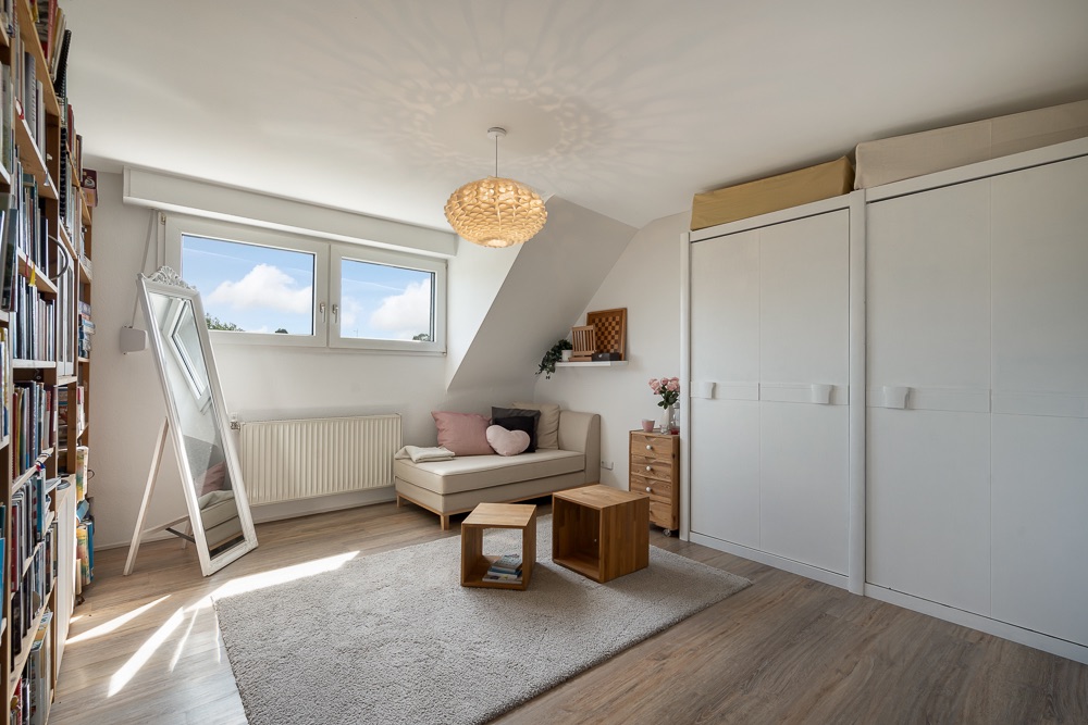 Helles Zimmer mit Sofa, großem Spiegel, Bücherregal und weißen Einbauschränken.