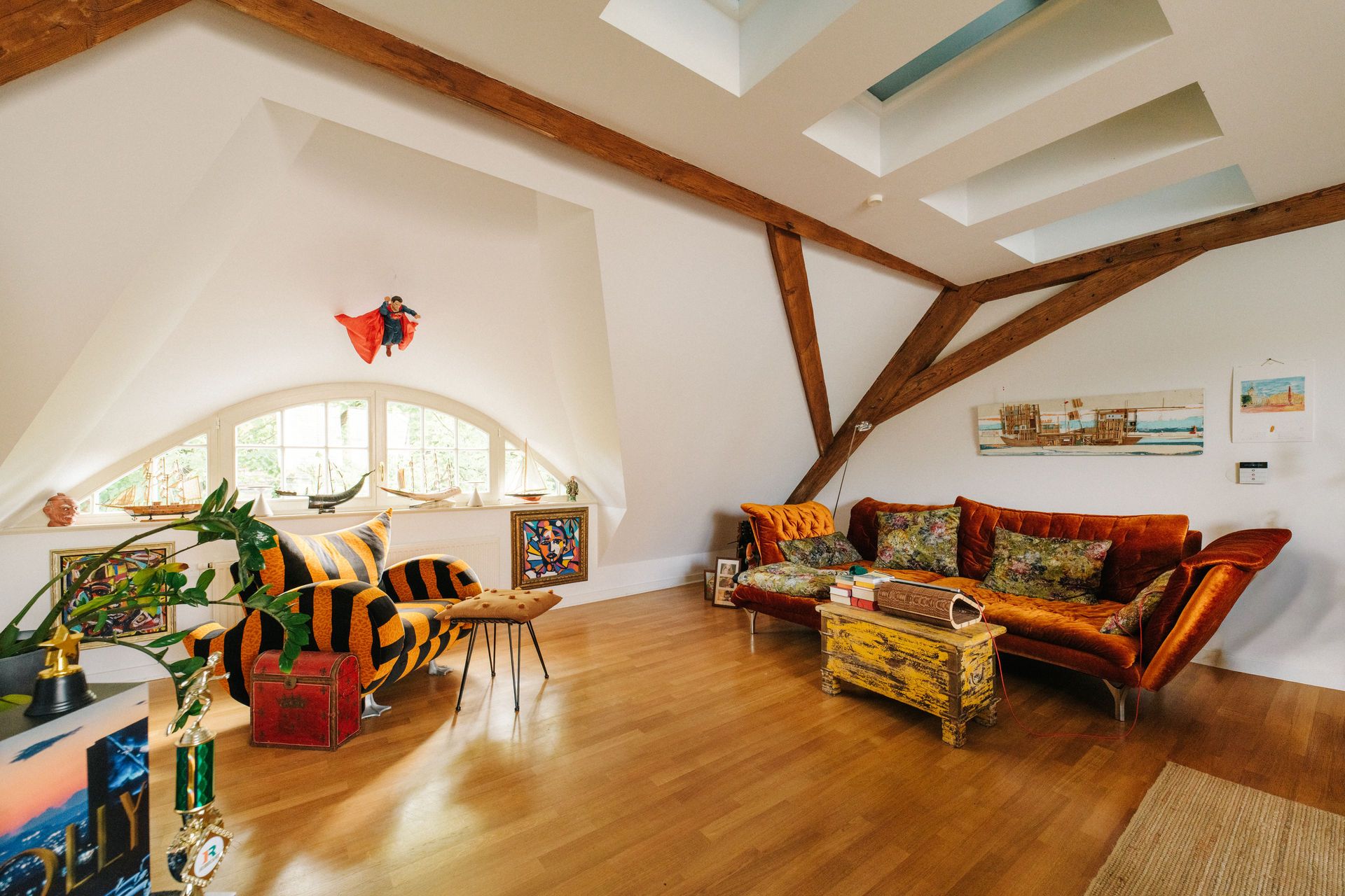 Wohnzimmer mit Holzfußboden, großen Fenstern, orangenem Sofa und Holzdecke mit Balken.