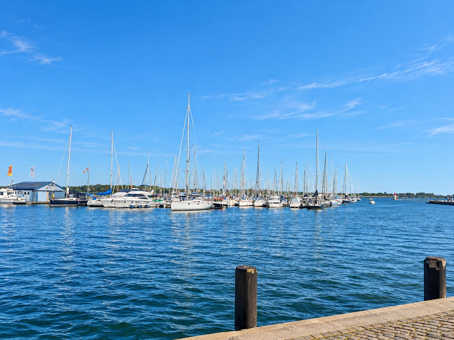 Blick auf einen Hafen mit vielen Segelbooten im Wasser bei blauem Himmel.