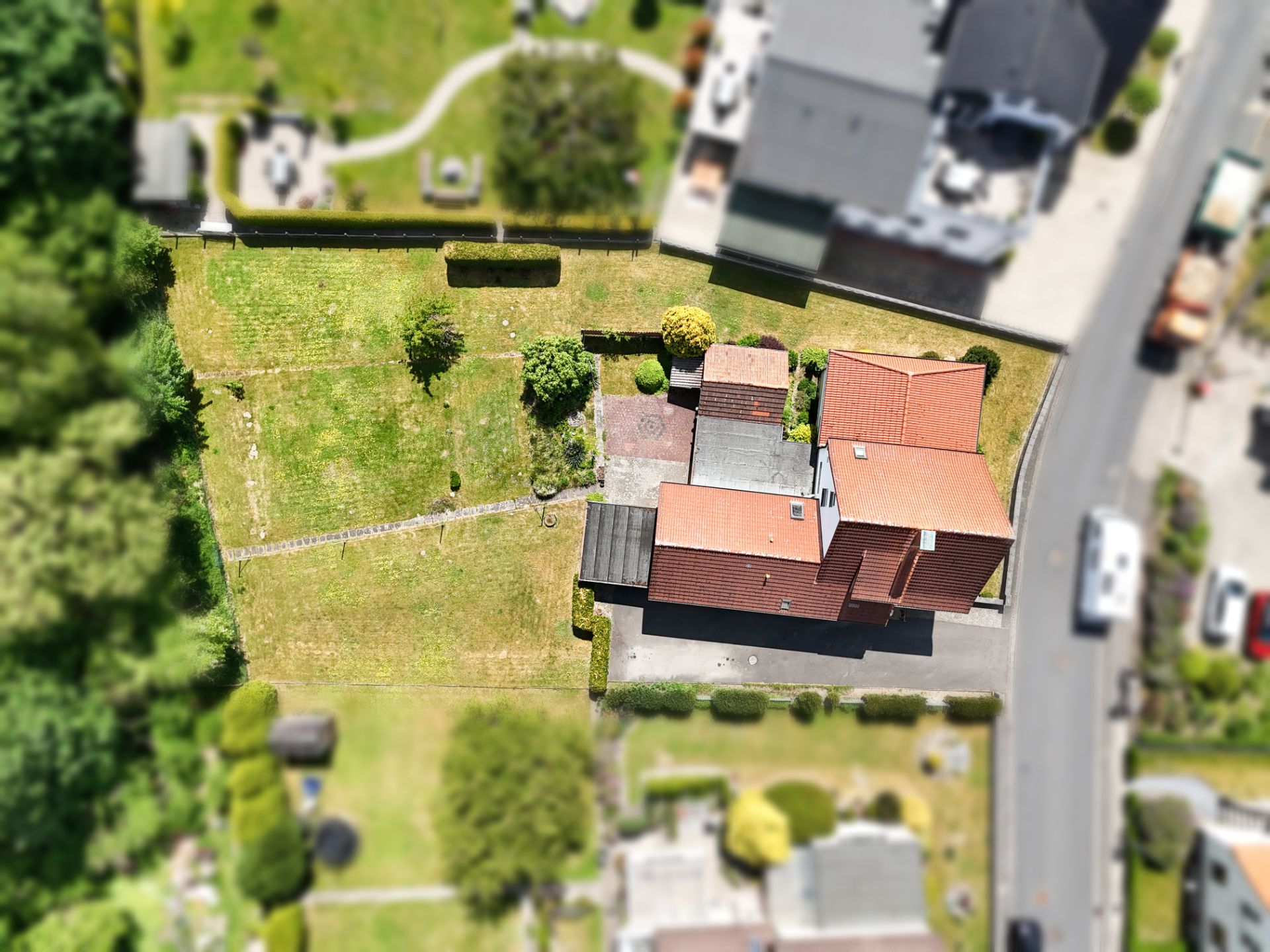 Luftaufnahme eines Einfamilienhauses mit rotem Dach und großem Garten an einer Straße.