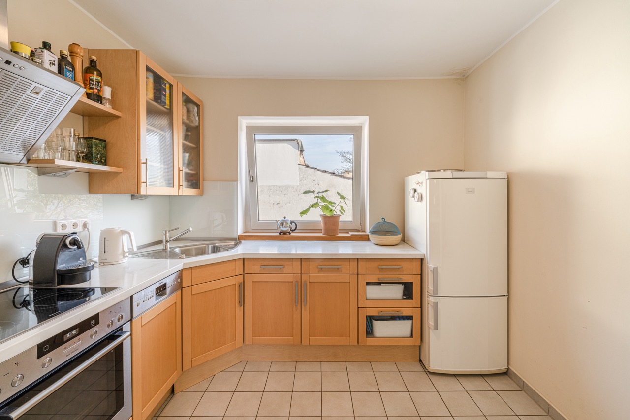 Helle Küche mit Holzschränken, Geräten, Fenster und großem weißen Kühlschrank.