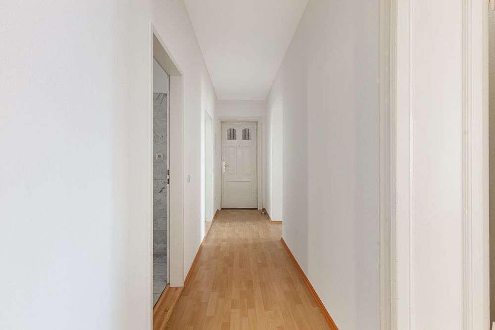 Heller Flur mit Holzboden und weißen Wänden, am Ende eine weiße Tür.