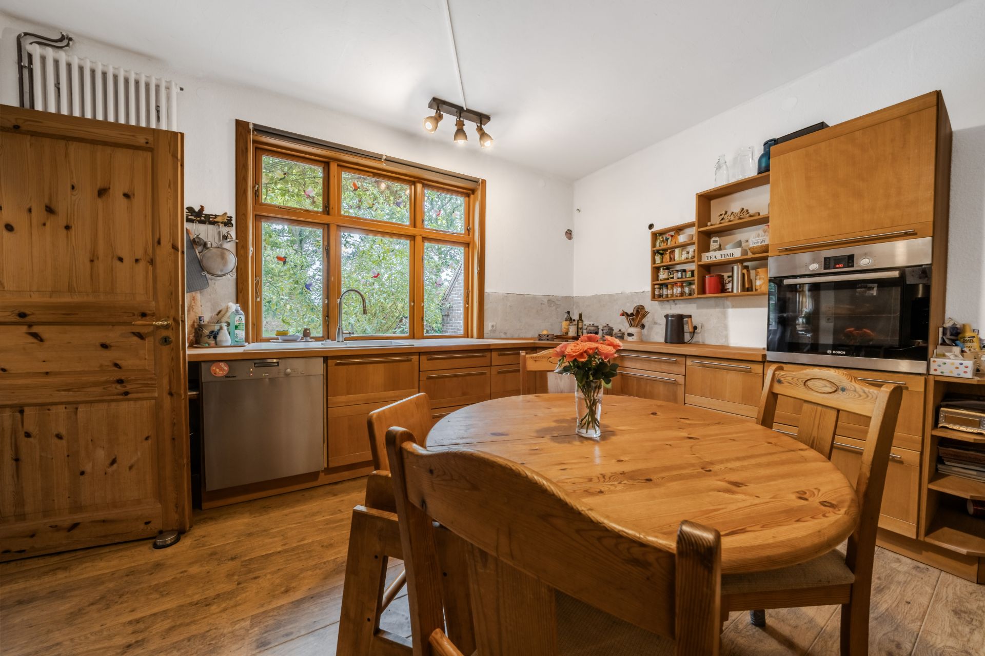 Gemütliche Holzküche mit rundem Tisch, Stühlen und großem Fenster im Hintergrund.