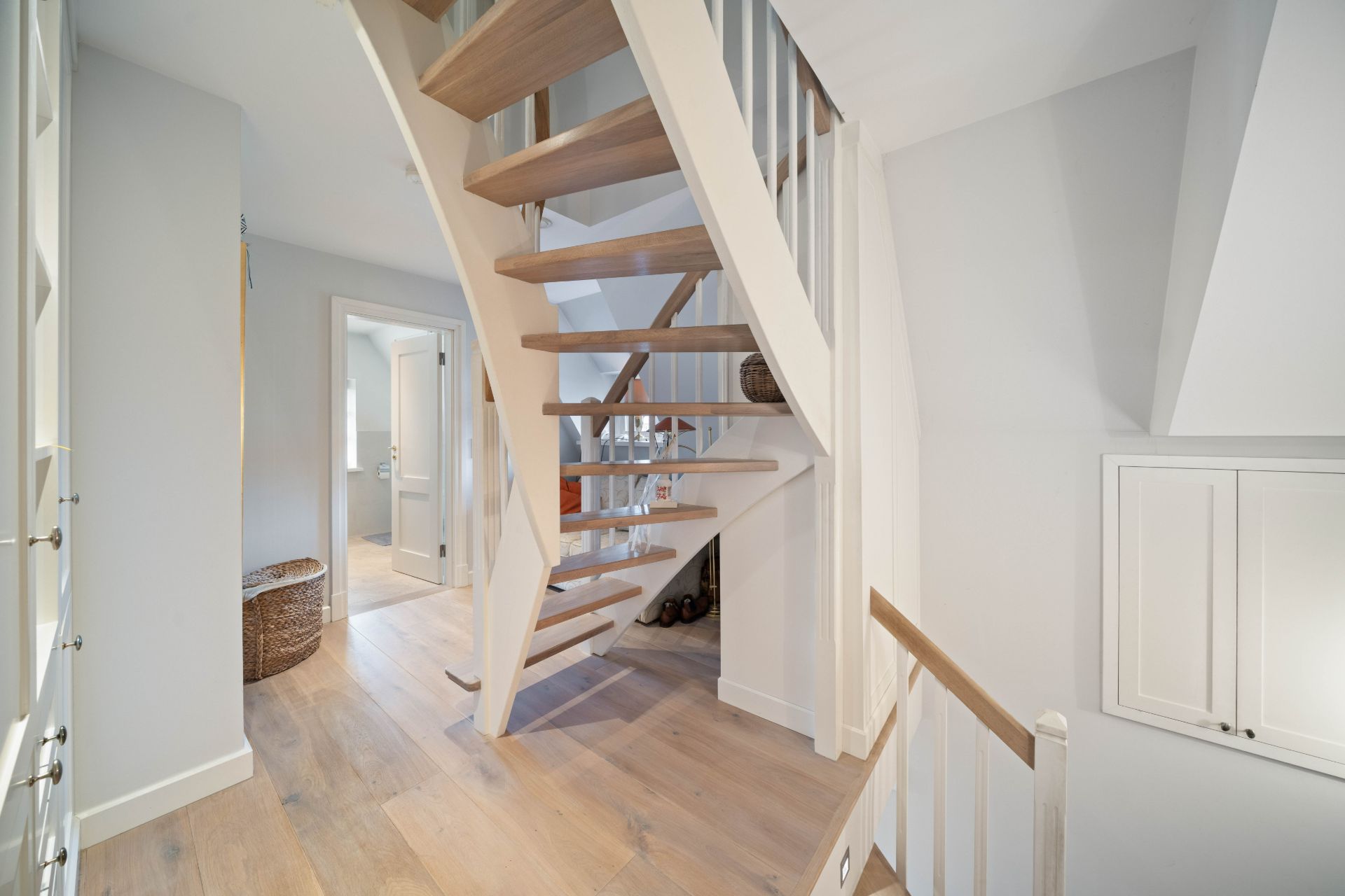 Heller Flur mit offener Holztreppe und hellem Holzboden in einem Wohnhaus.