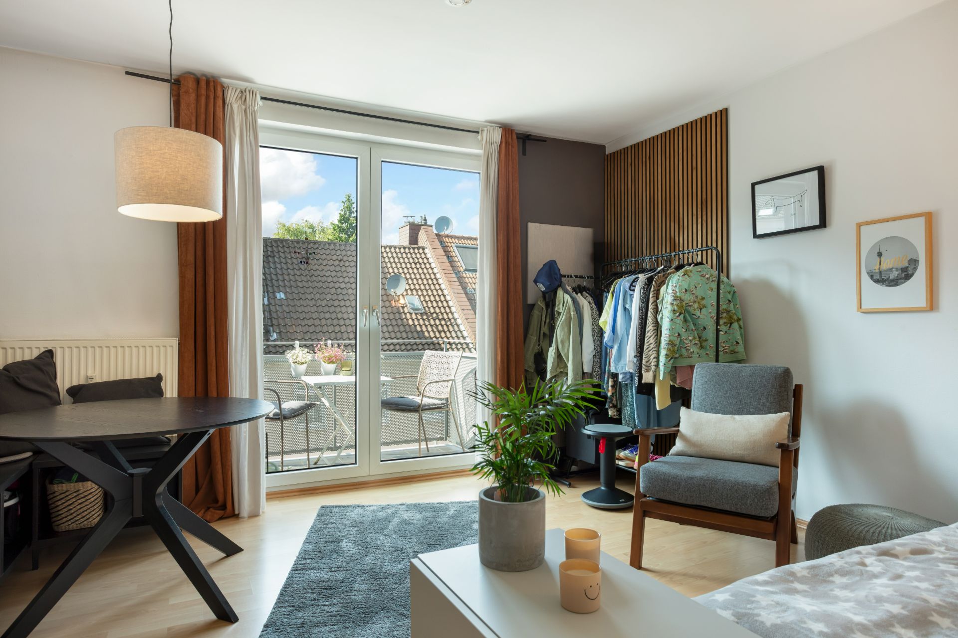 Helles Wohnzimmer mit Glastür zum Balkon, Esstisch, Sessel und Kleiderstange.