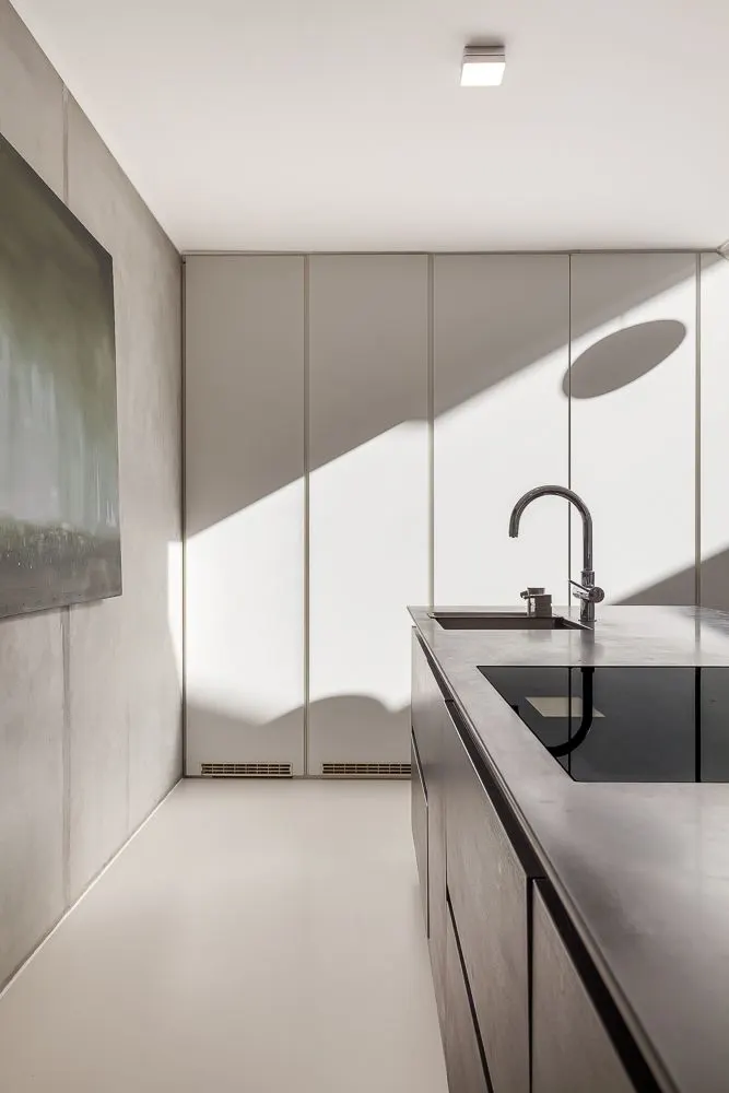 Moderne Küche mit Kochinsel, Wasserhahn, großem Gemälde und heller Wand mit Schatten.