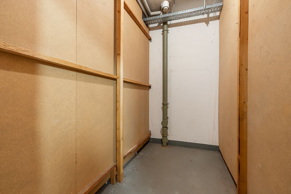 Schlichter Abstellraum mit Holzwänden, grauem Boden und sichtbarem Rohr an der Wand.