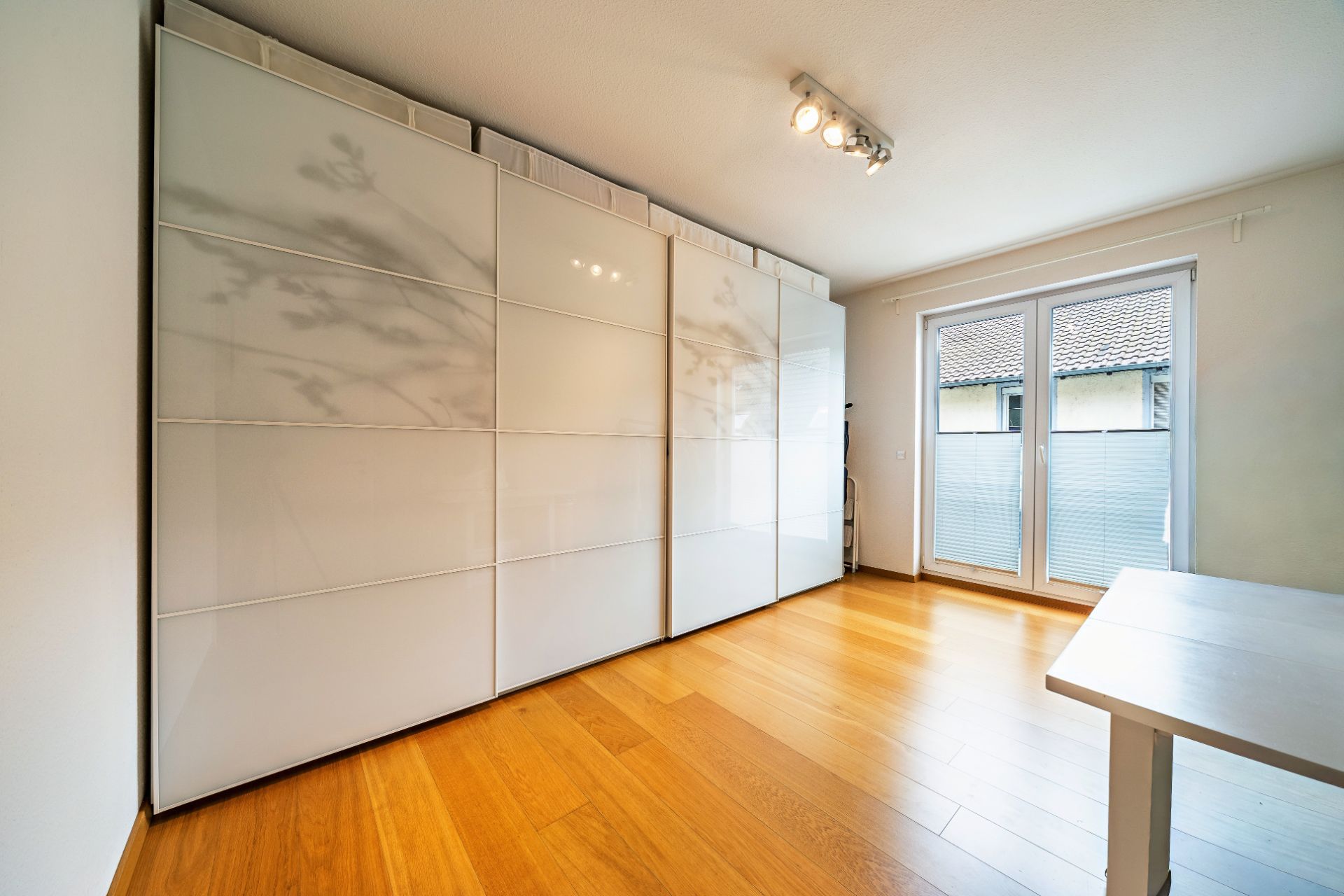 Helles Zimmer mit großem weißen Kleiderschrank, Holzboden und Glastür zum Balkon.