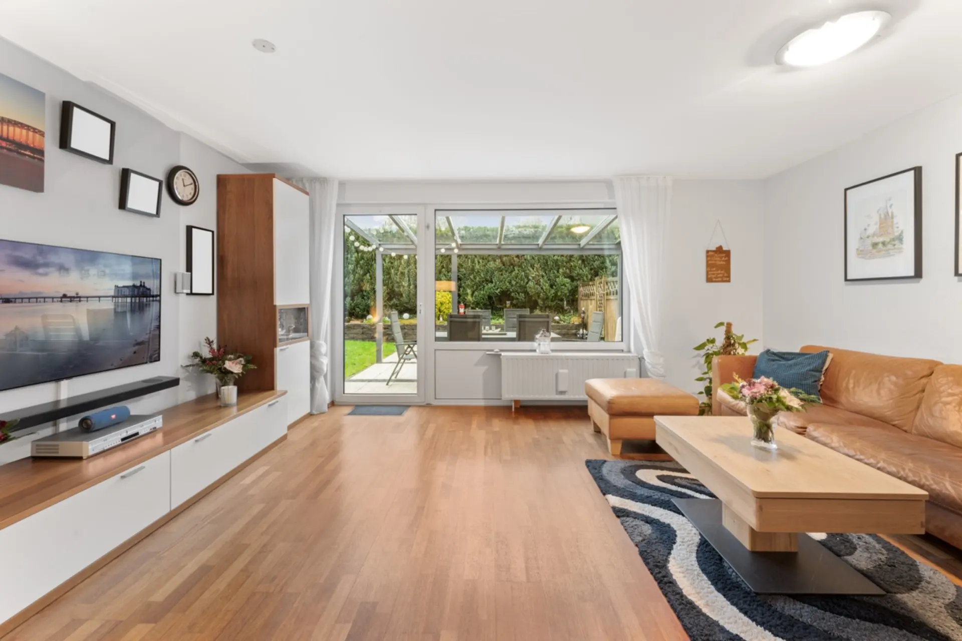 Helles Wohnzimmer mit Ledercouch, Holztisch und Blick auf Terrasse und Garten.