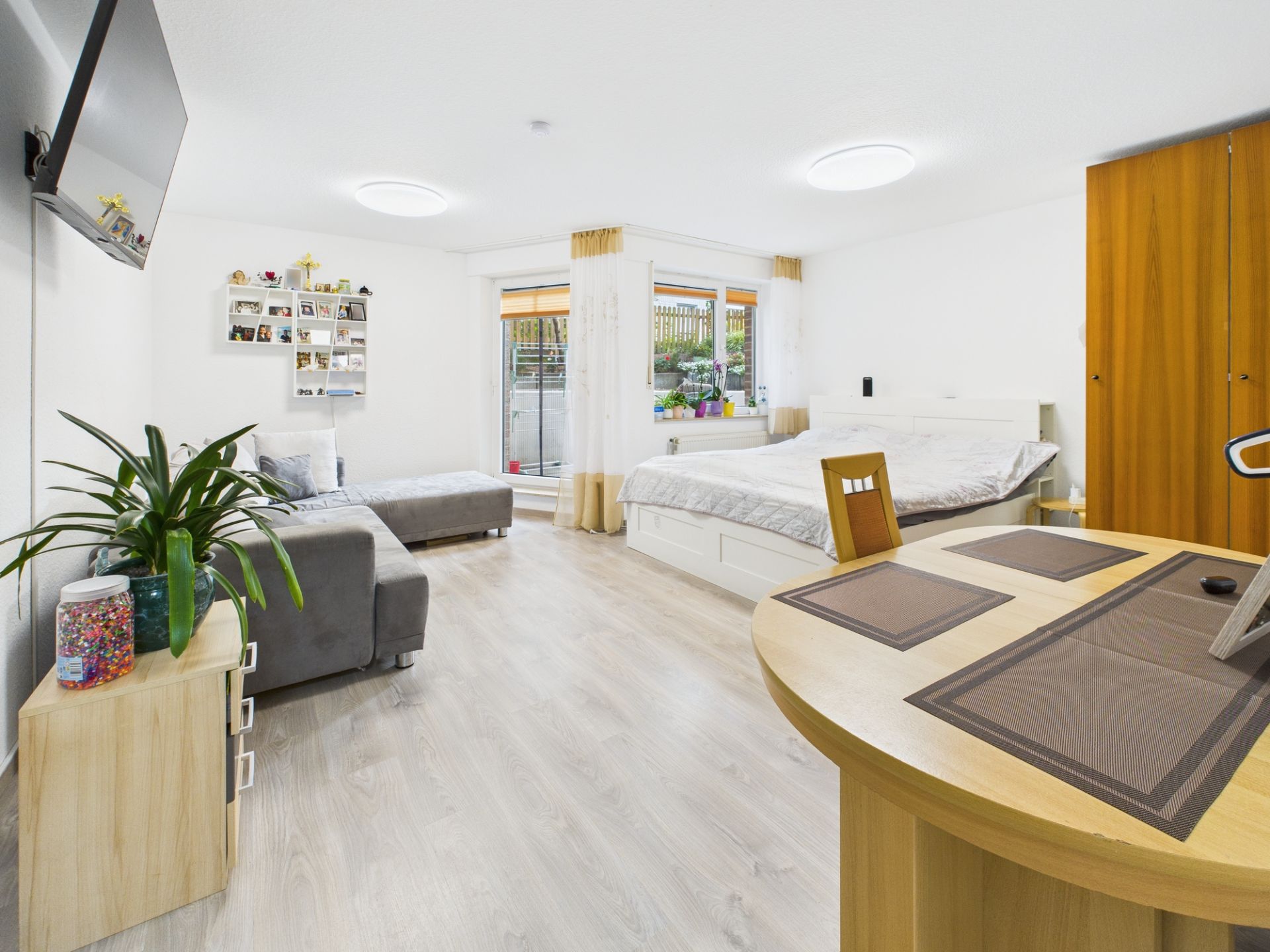 Helles Wohn- und Schlafzimmer mit Bett, Sofa, Tisch, Schrank und großem Fenster.