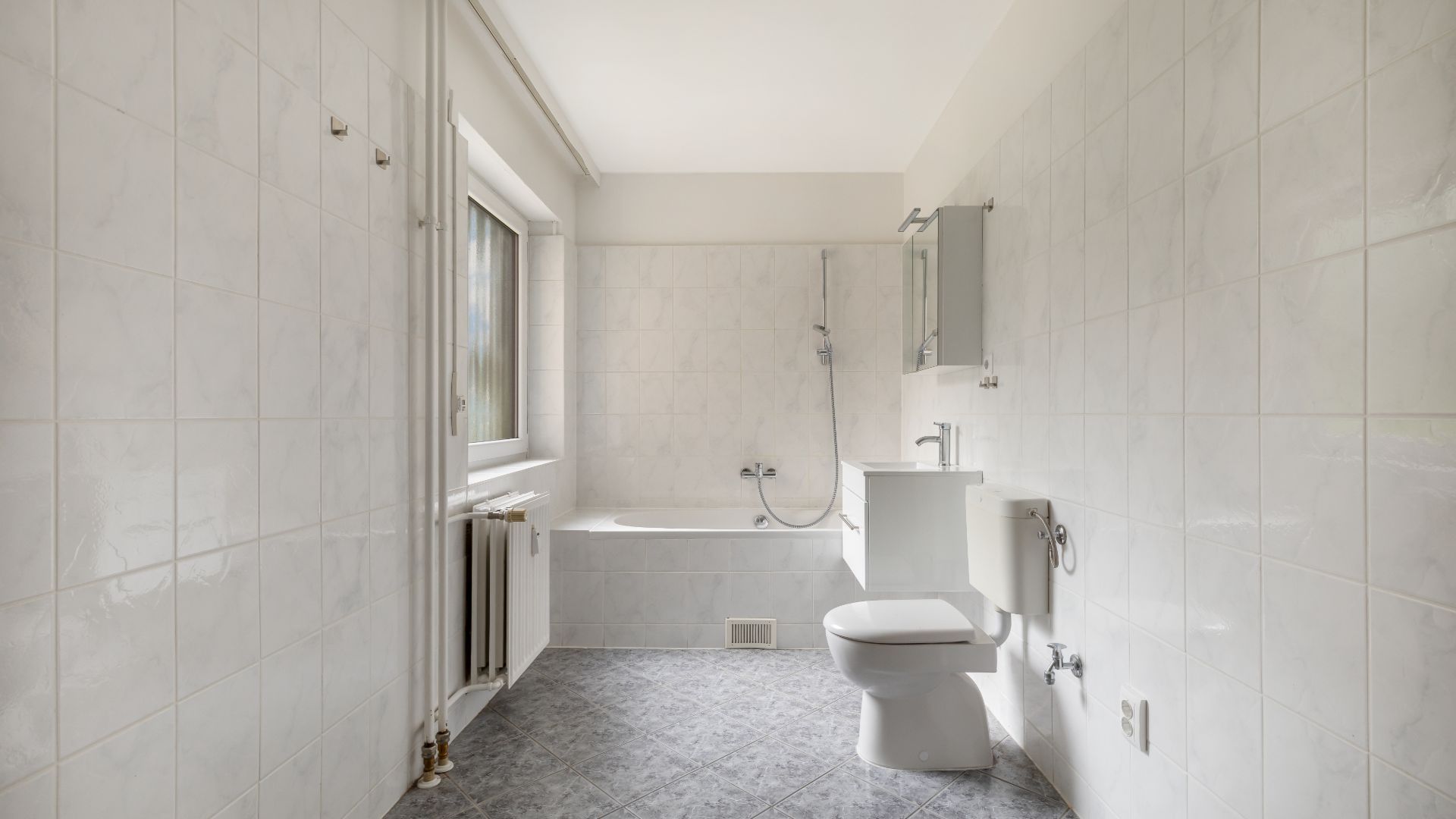 Helles Badezimmer mit Badewanne, WC, Waschbecken und Fenster.