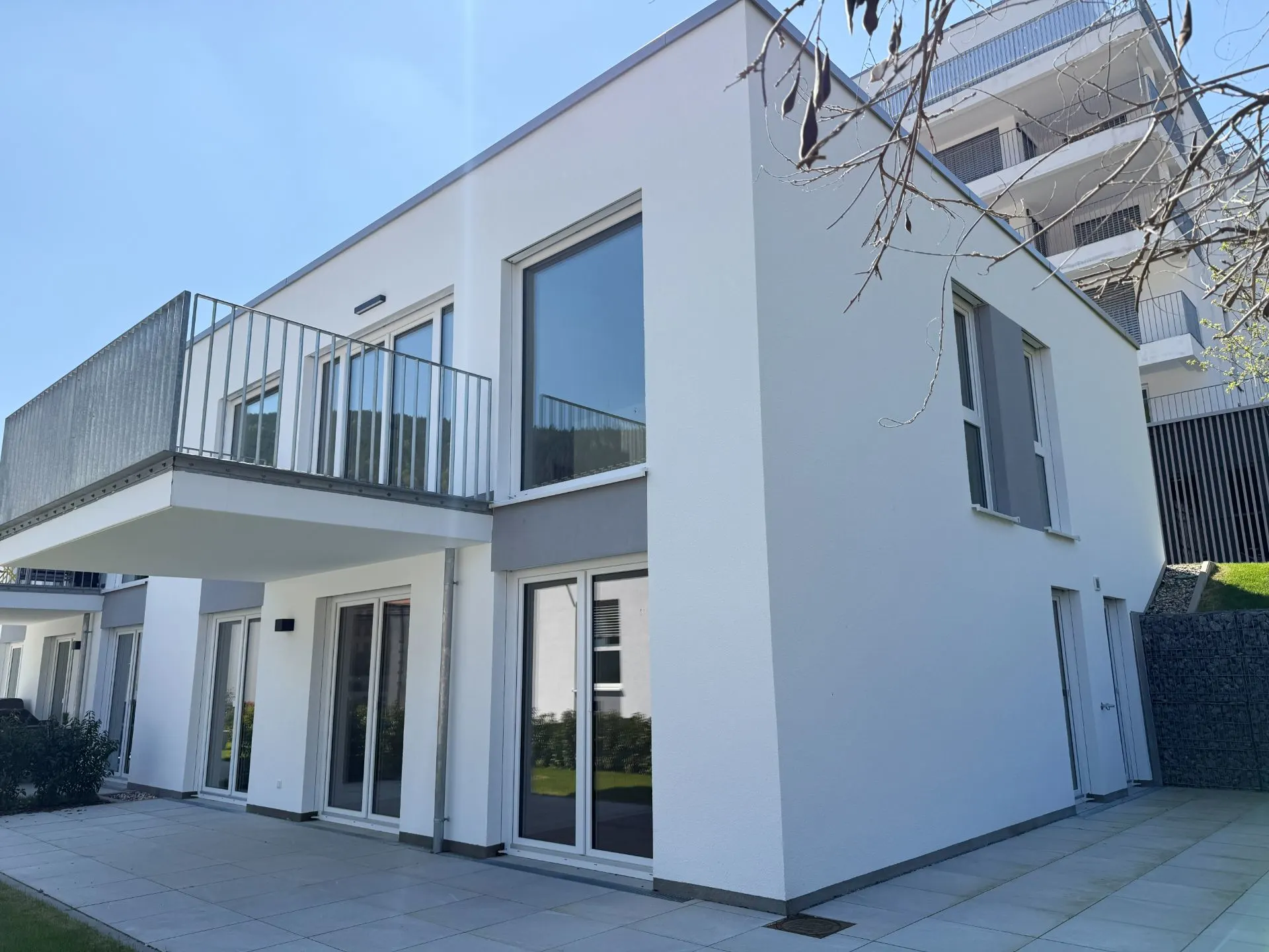 Modernes, weißes Wohnhaus mit großen Fenstern, Balkon und Terrasse.