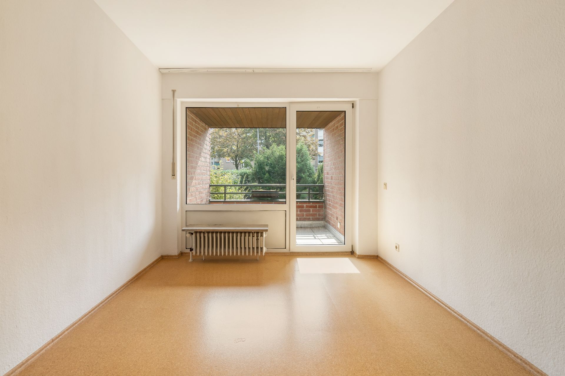 Leerer Raum mit Fenster und Tür zu einem kleinen Balkon, Heizkörper unter dem Fenster.