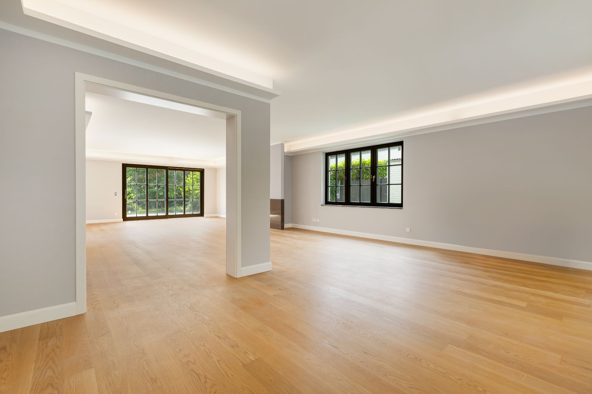 Helles, leeres Wohnzimmer mit Holzfußboden und großen Fenstern.