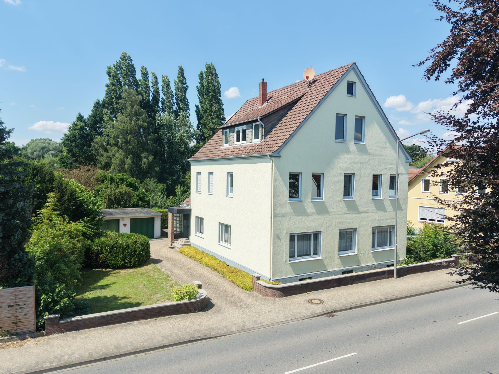 Zweistöckiges, helles Wohnhaus mit Satteldach, Vorgarten und Auffahrt an einer Straße.