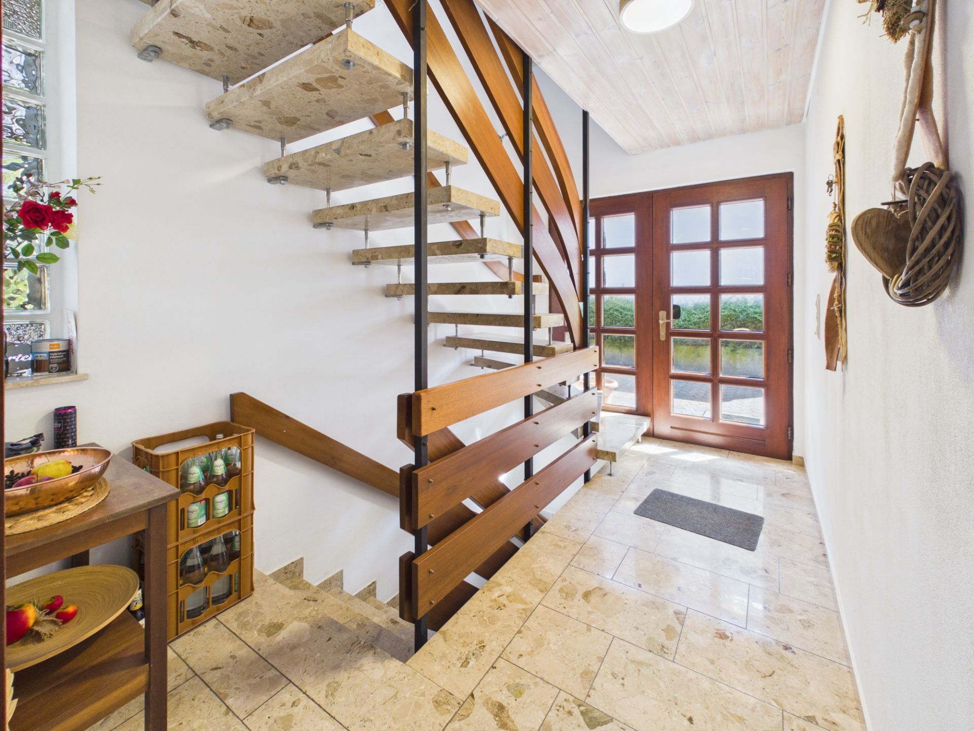 Heller Flur mit Natursteintreppe, Holztüren und kleinen Regalen an der Seite.