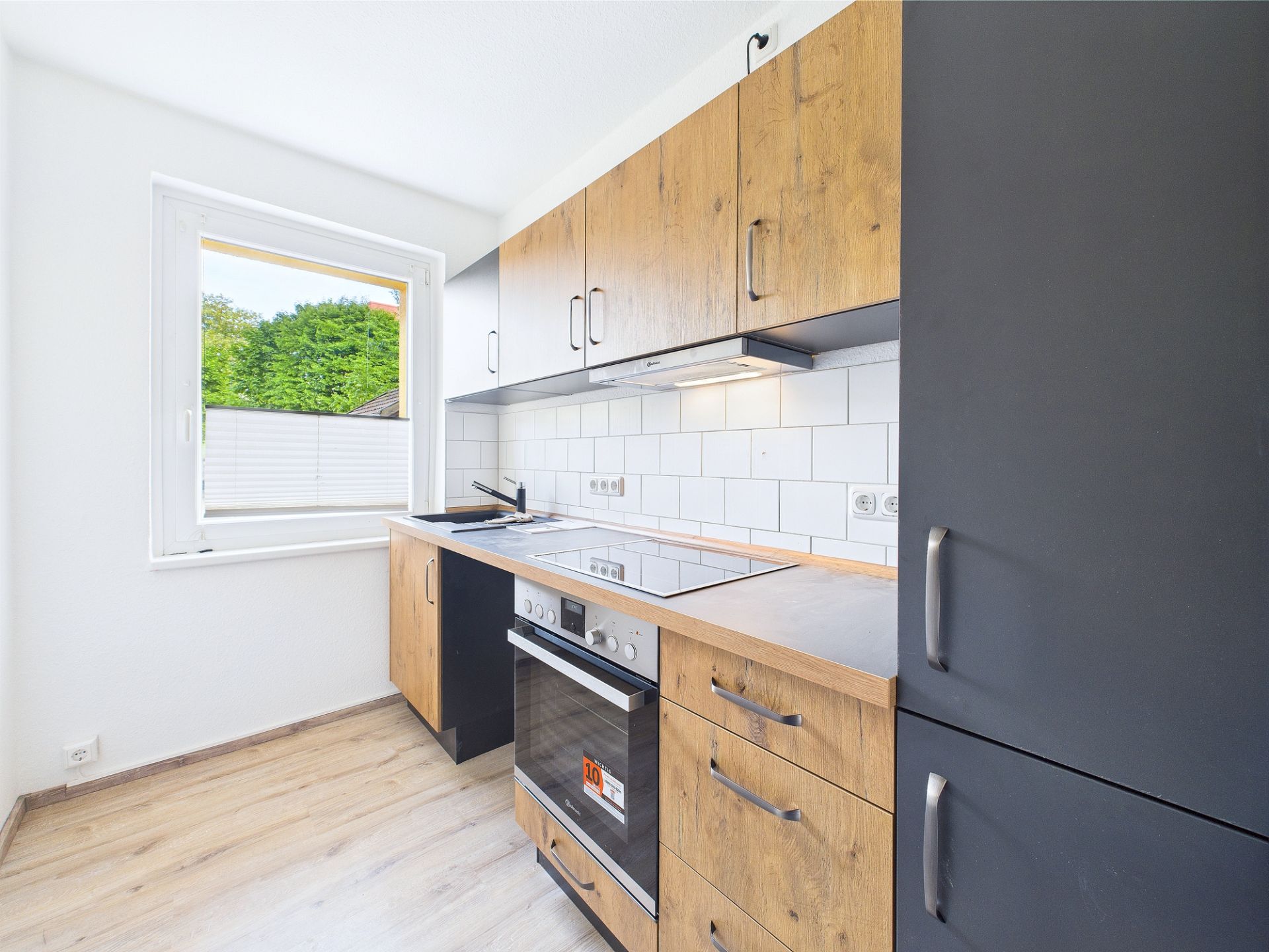 Moderne Küche mit Holzfronten, Herd, Spüle, weißen Fliesen und großem Fenster.