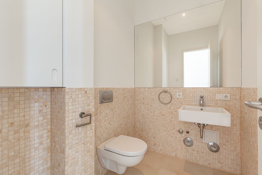 Modernes Badezimmer mit Wandtoilette, kleinem Waschbecken und großem Spiegel.