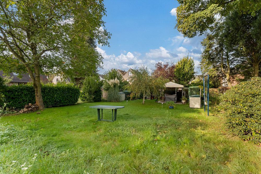 Großer Garten mit Bäumen, Rasenfläche, Rundtisch und Pavillon im Hintergrund.
