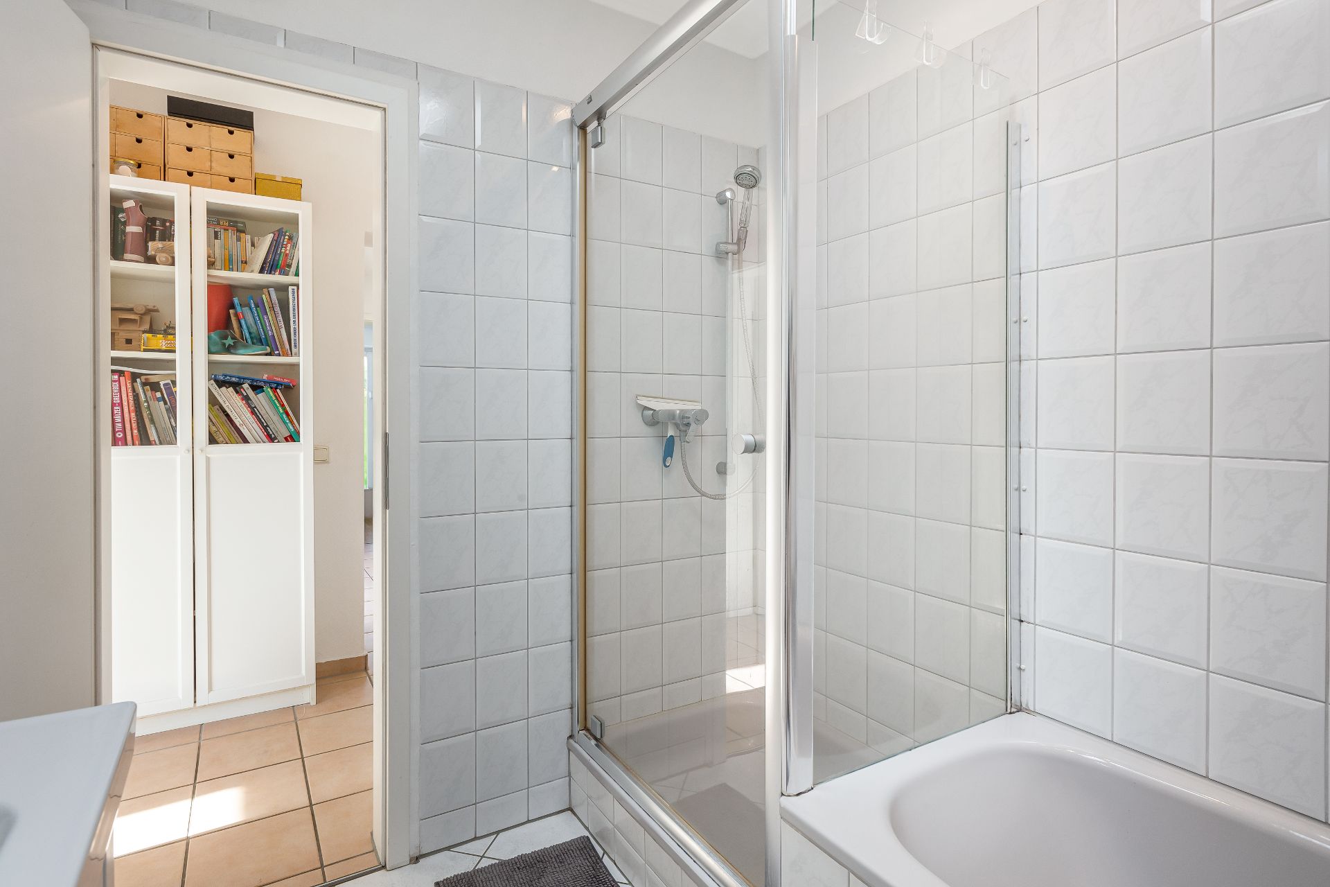 Helles Badezimmer mit Dusche, Badewanne und Blick auf ein Bücherregal im Flur.